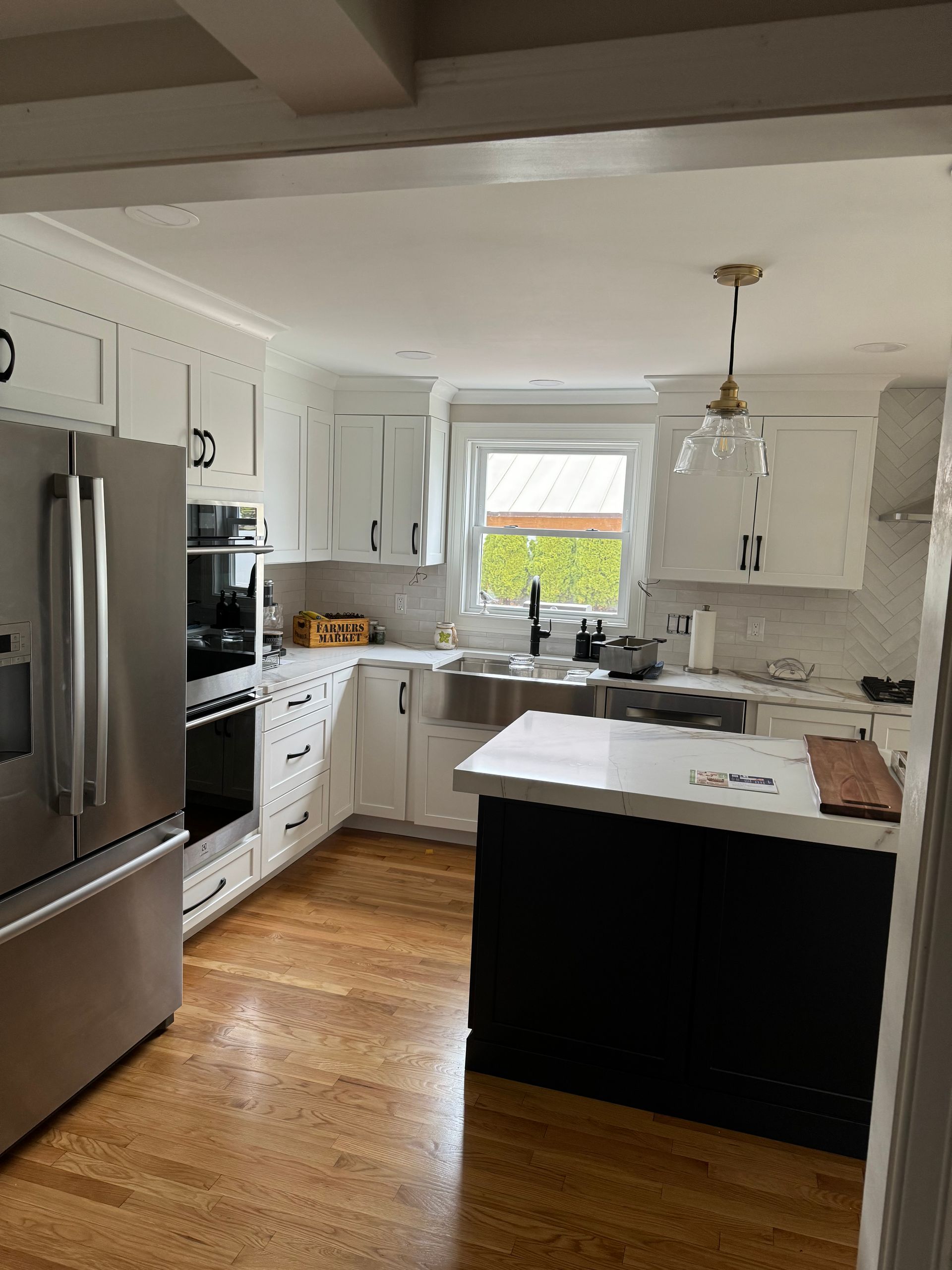Bright modern kitchen with stainless fridge, white cabinets, wood floor, and a black island by a window.
