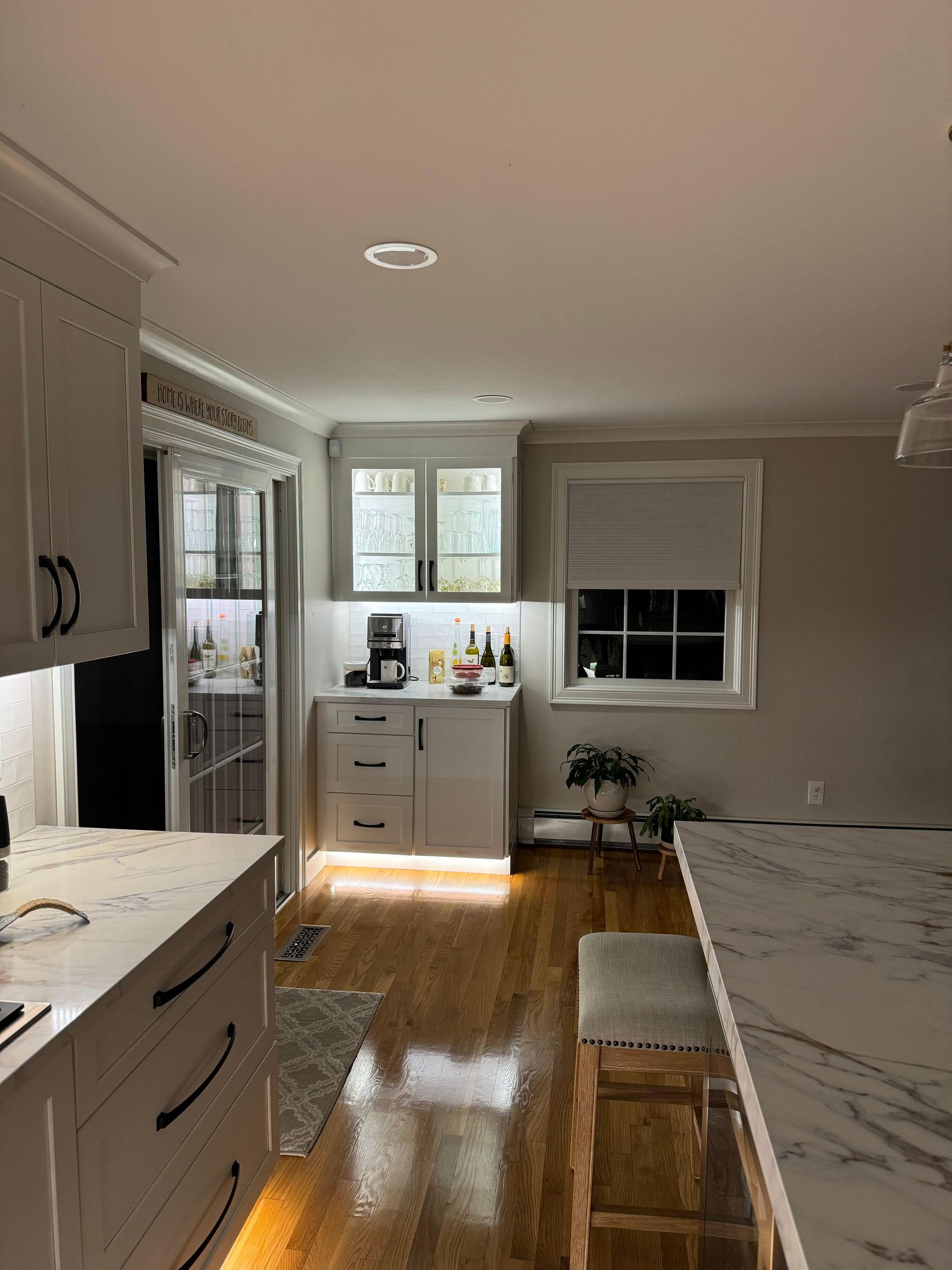 Bright kitchen with white cabinets, wood floors, and sunlight by a window and small dining area.