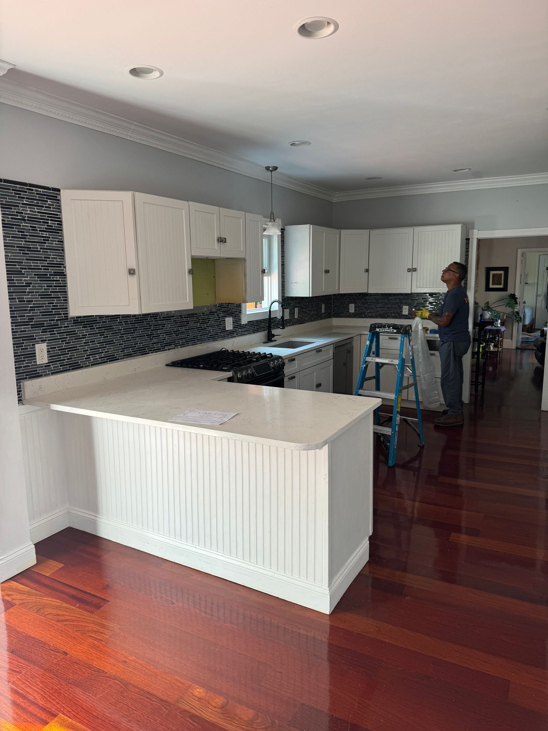 Modern kitchen with white cabinets, black tile backsplash, and a large white island on a hardwood floor