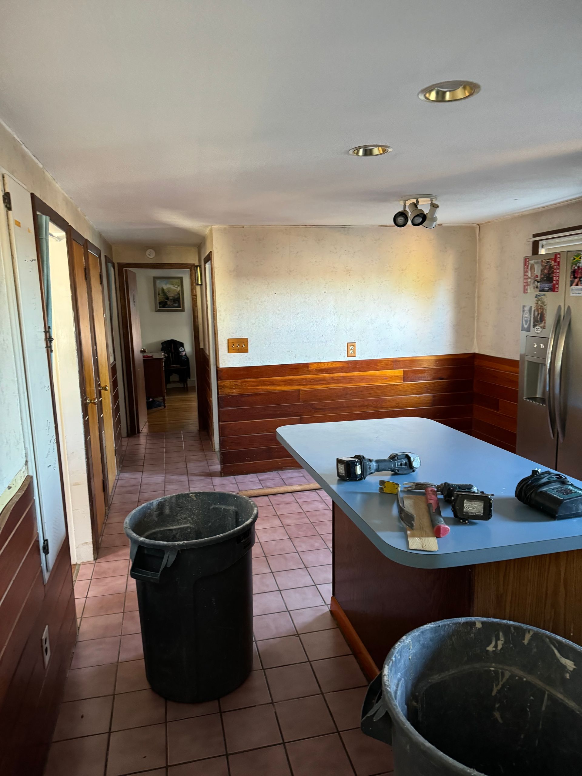 Empty room with tiled floor, wood-paneled walls, and a countertop table in the foreground.