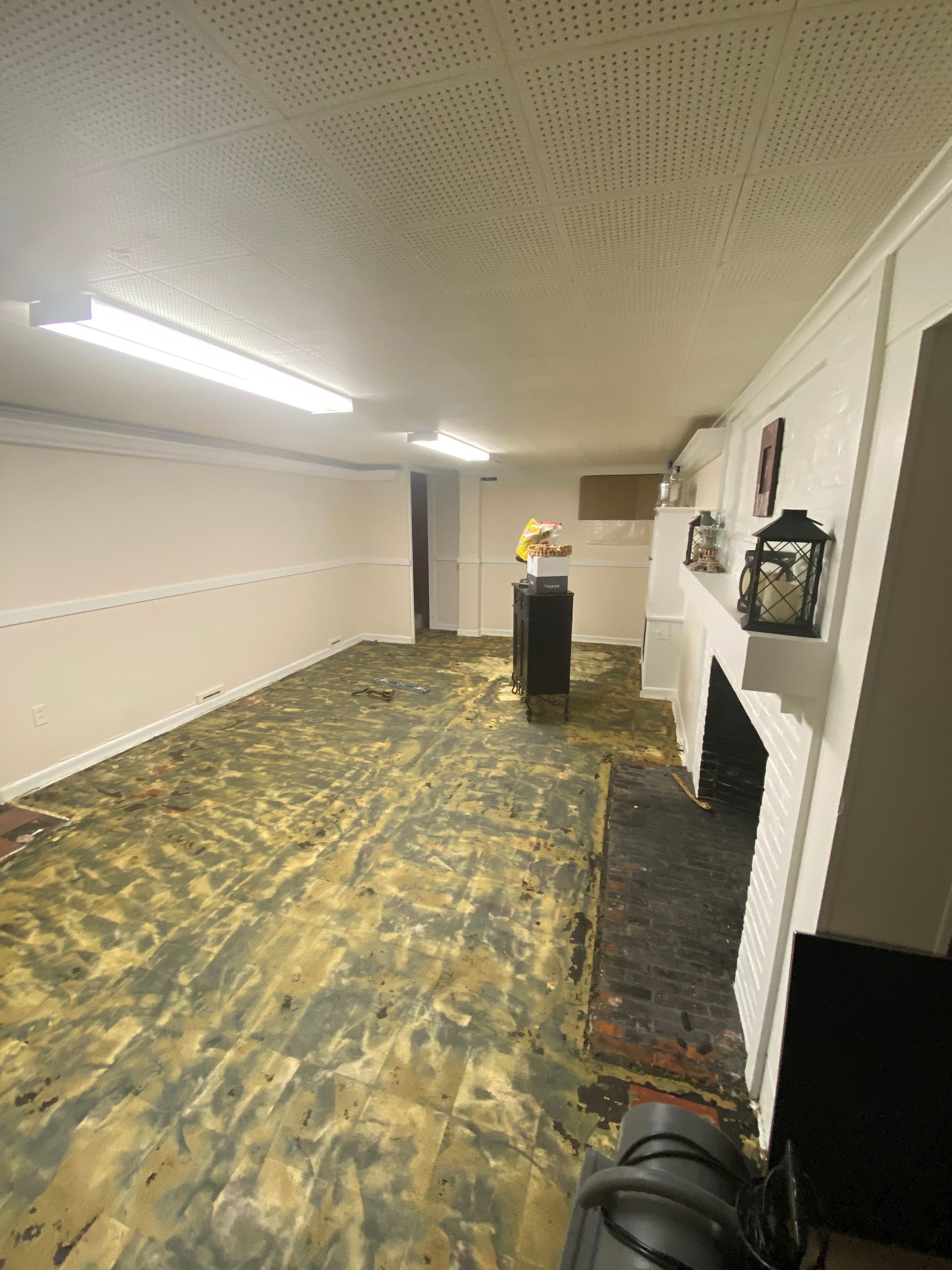 Empty long room with yellow-stained carpet, white walls, fluorescent lights, and a small podium at the far end