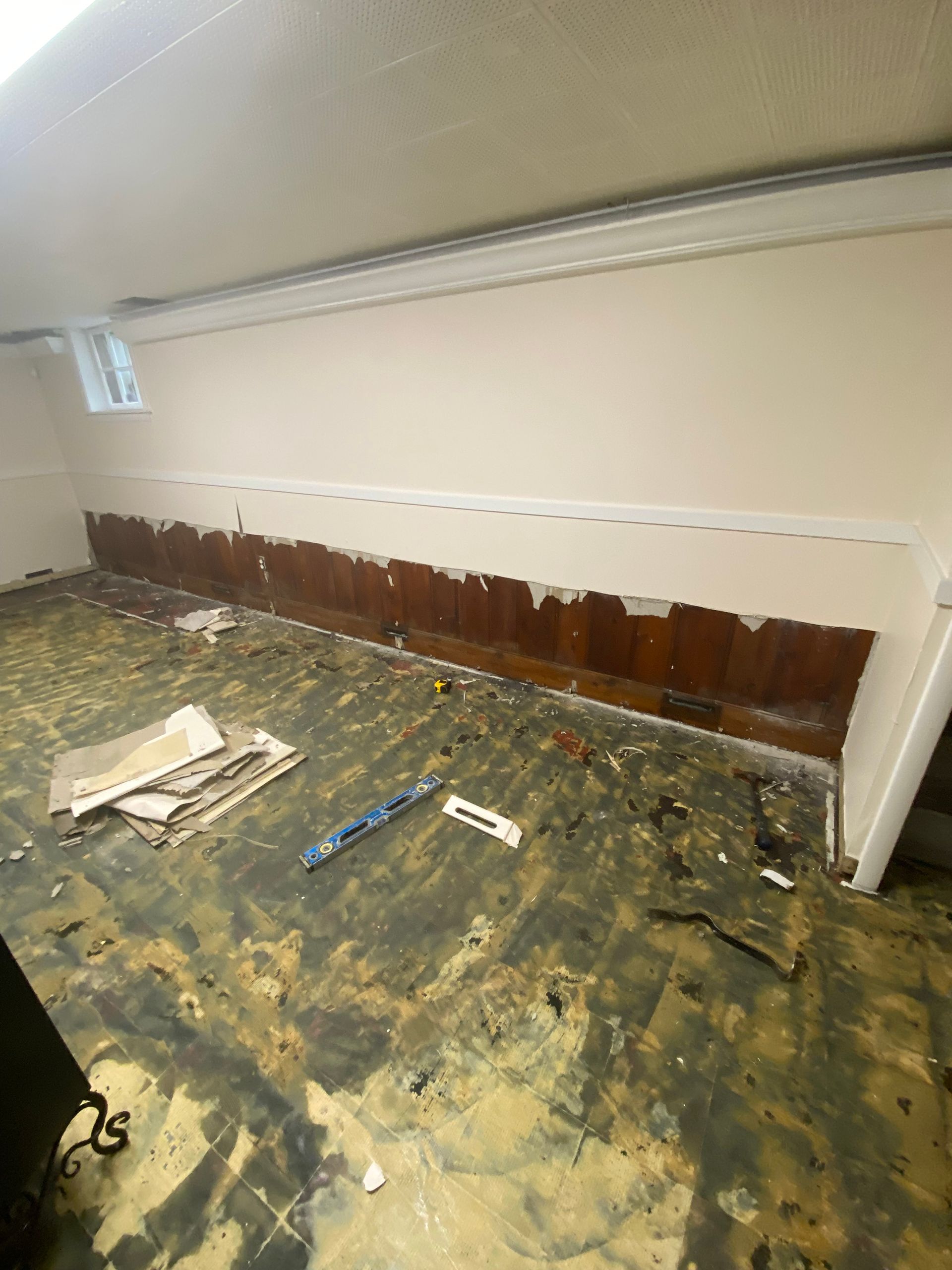 Damaged room wall with exposed brown paneling and debris scattered across a stained floor