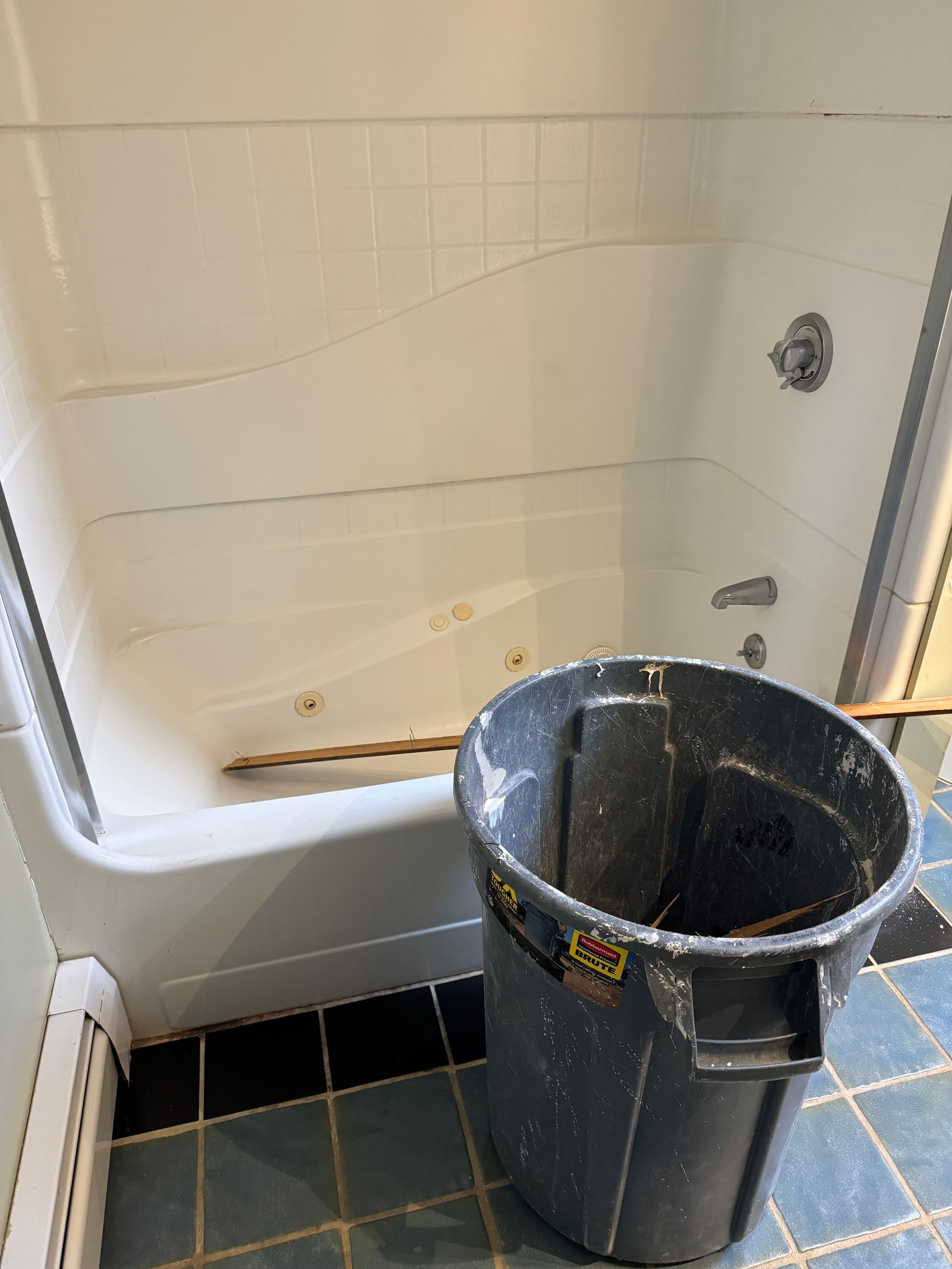 White bathtub with cracked surface and a black bucket in front, in a tiled bathroom