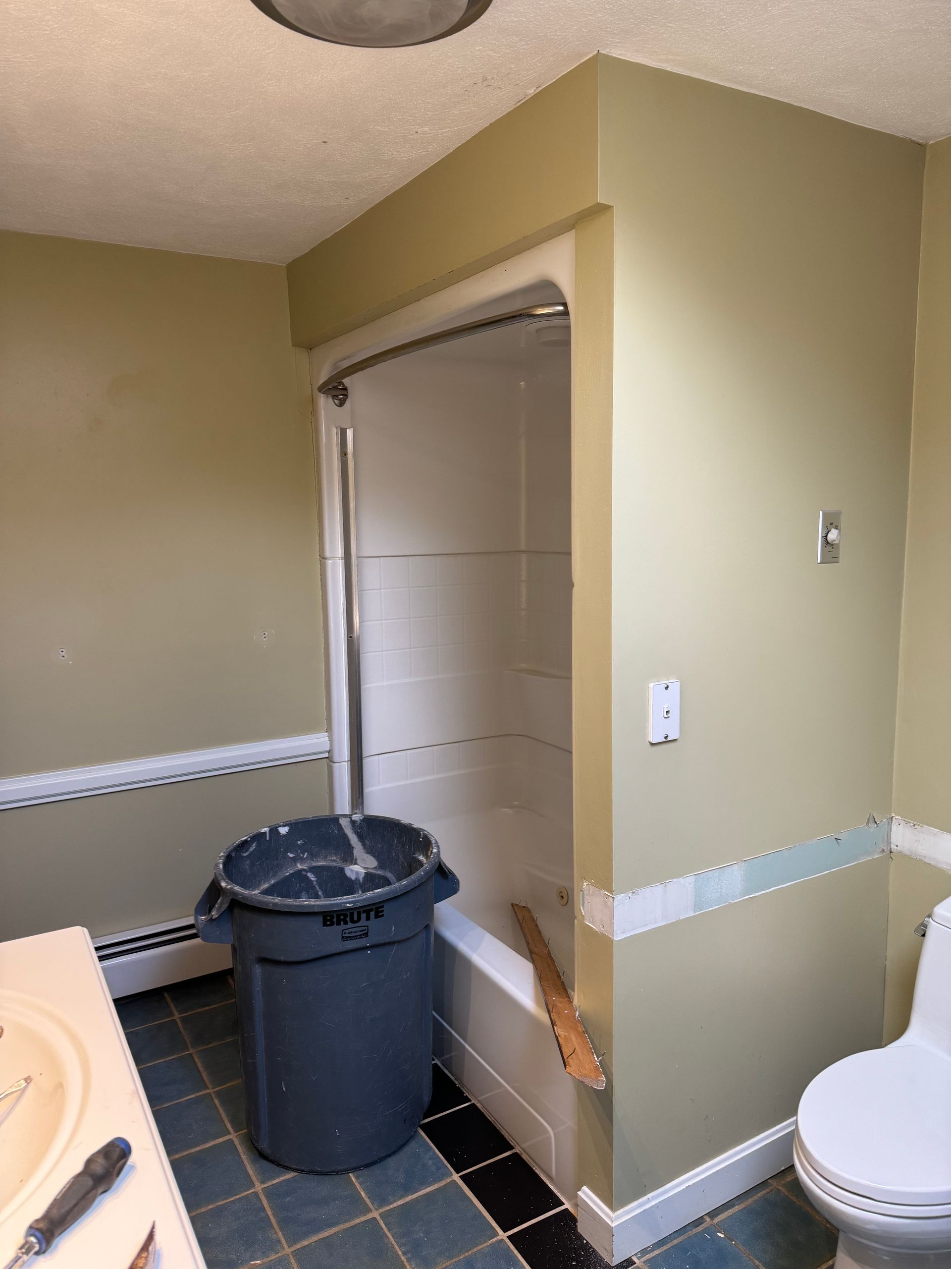 Small bathroom with a toilet, trash can, and open shower stall; beige walls and black tile floor.