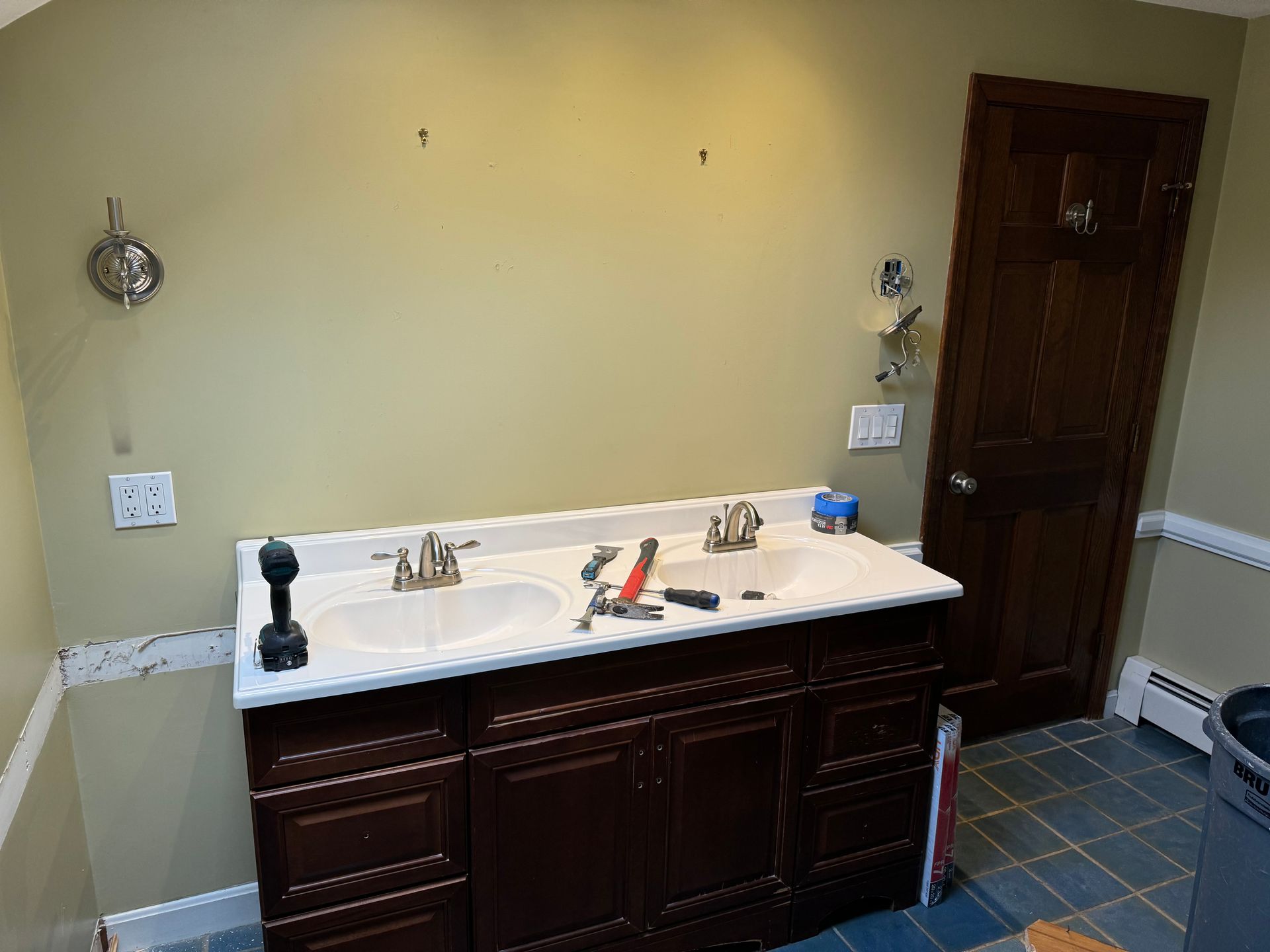 Bathroom vanity with double sink, dark wood cabinets, beige walls, and blue tile floor
