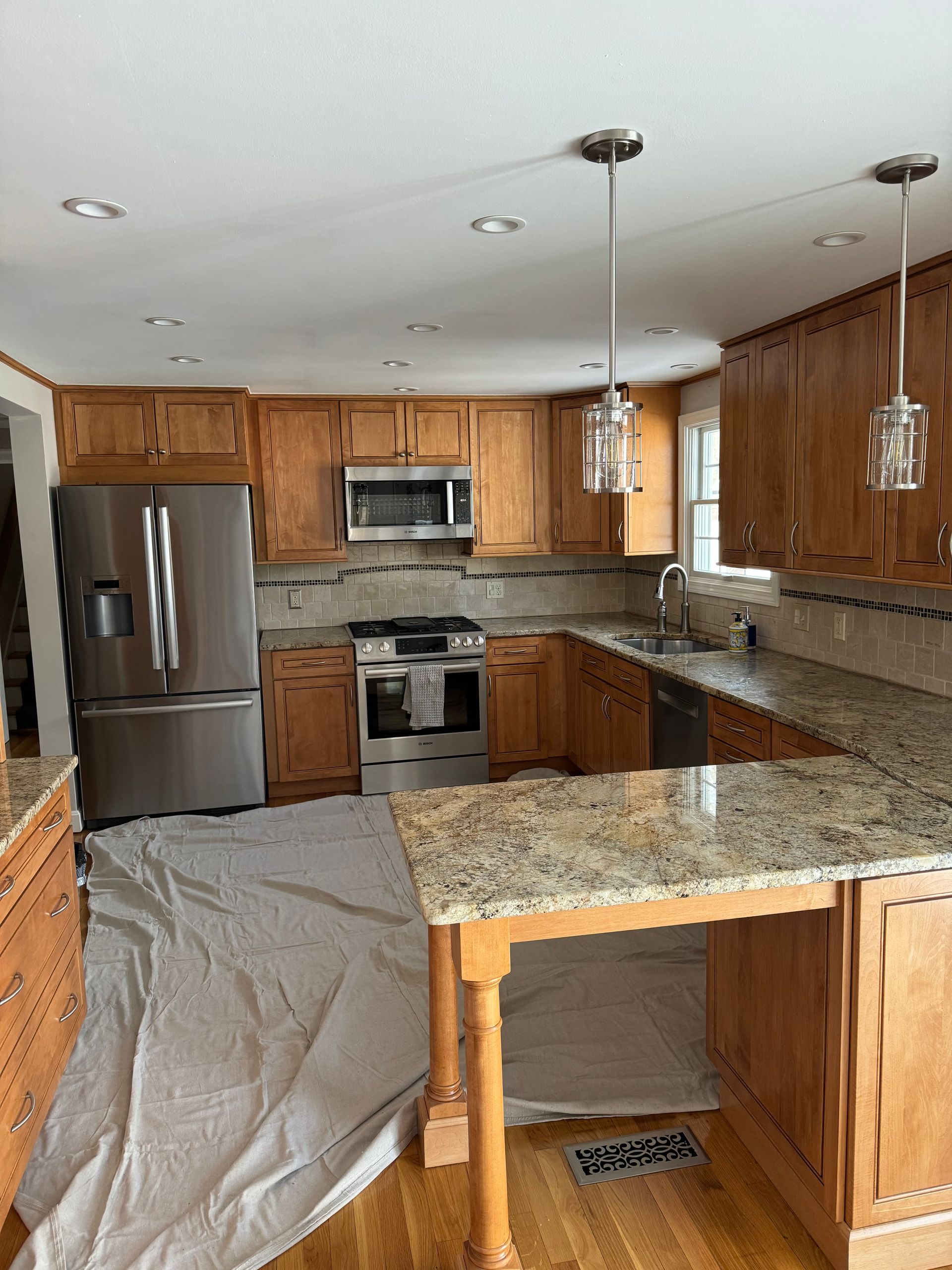 Kitchen under renovation with stainless steel appliances, wooden cabinets, granite counters, and covered floor.