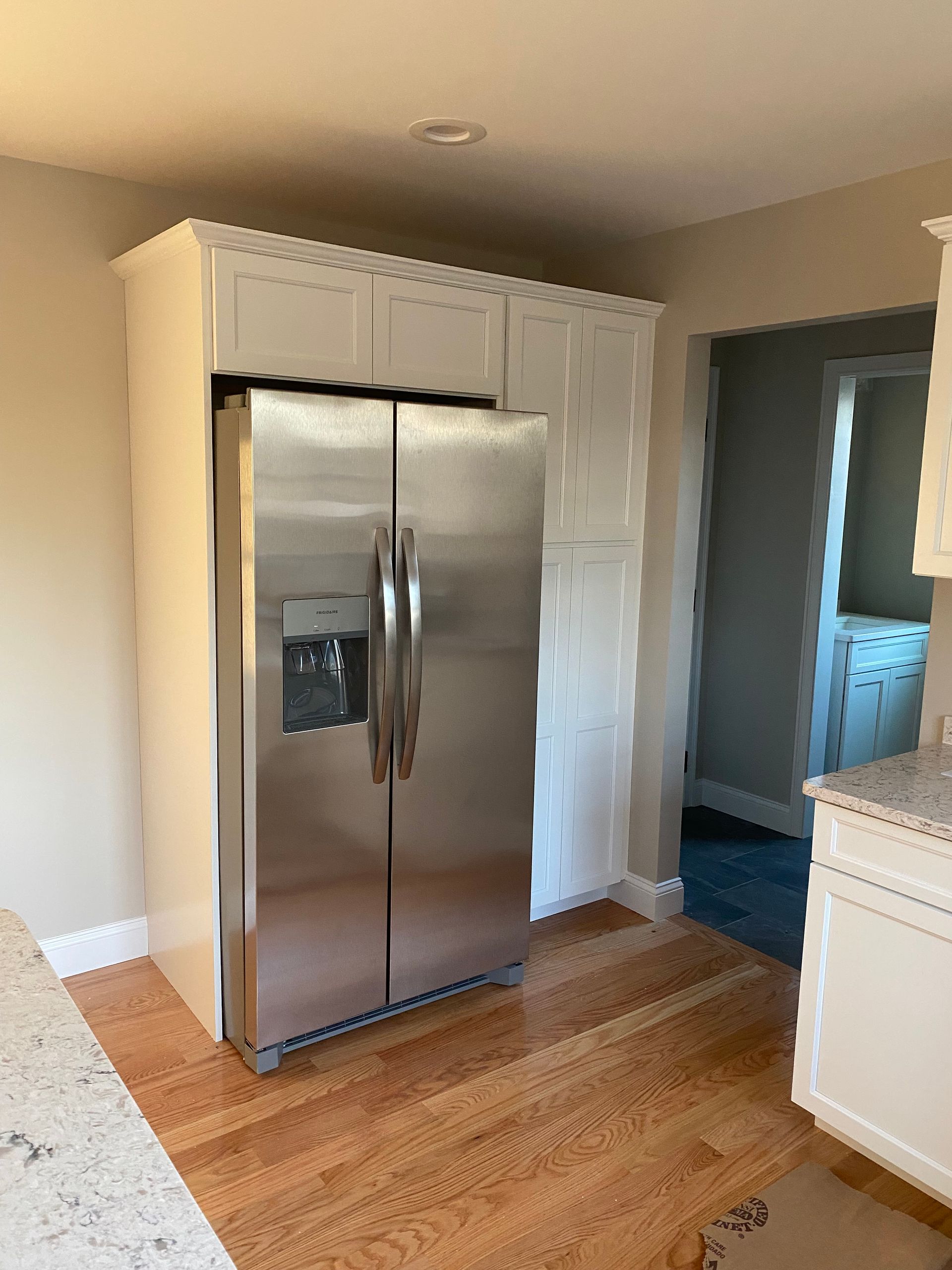 A stainless steel refrigerator is sitting in a kitchen next to a wooden floor