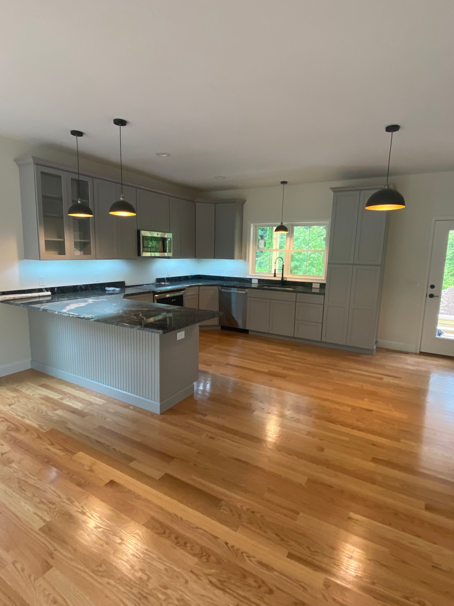 An empty kitchen with hardwood floors and gray cabinets