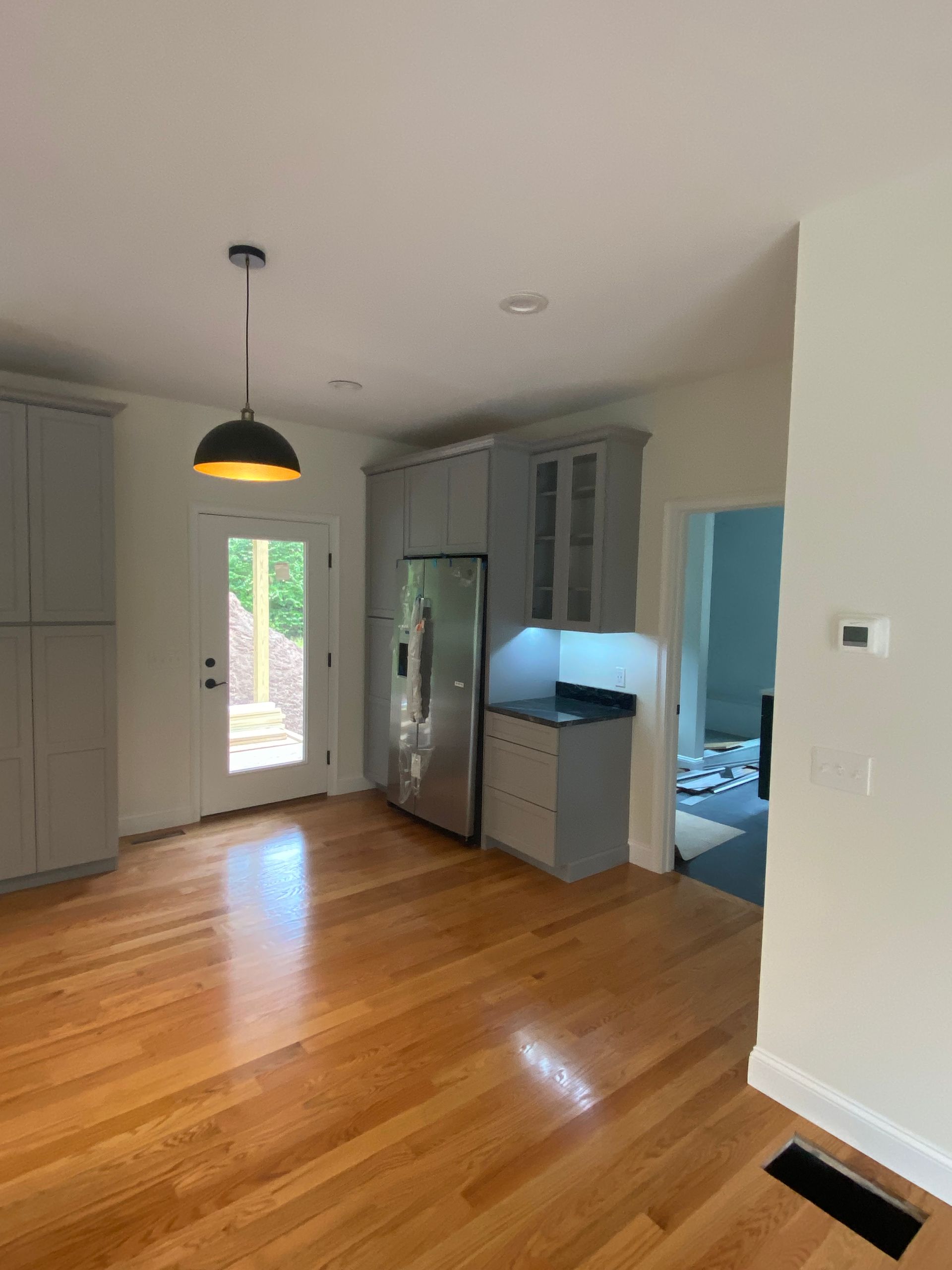 An empty kitchen with hardwood floors and a stainless steel refrigerator