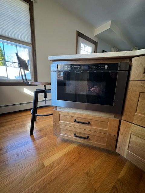 A microwave oven is sitting on top of a wooden cabinet in a kitchen