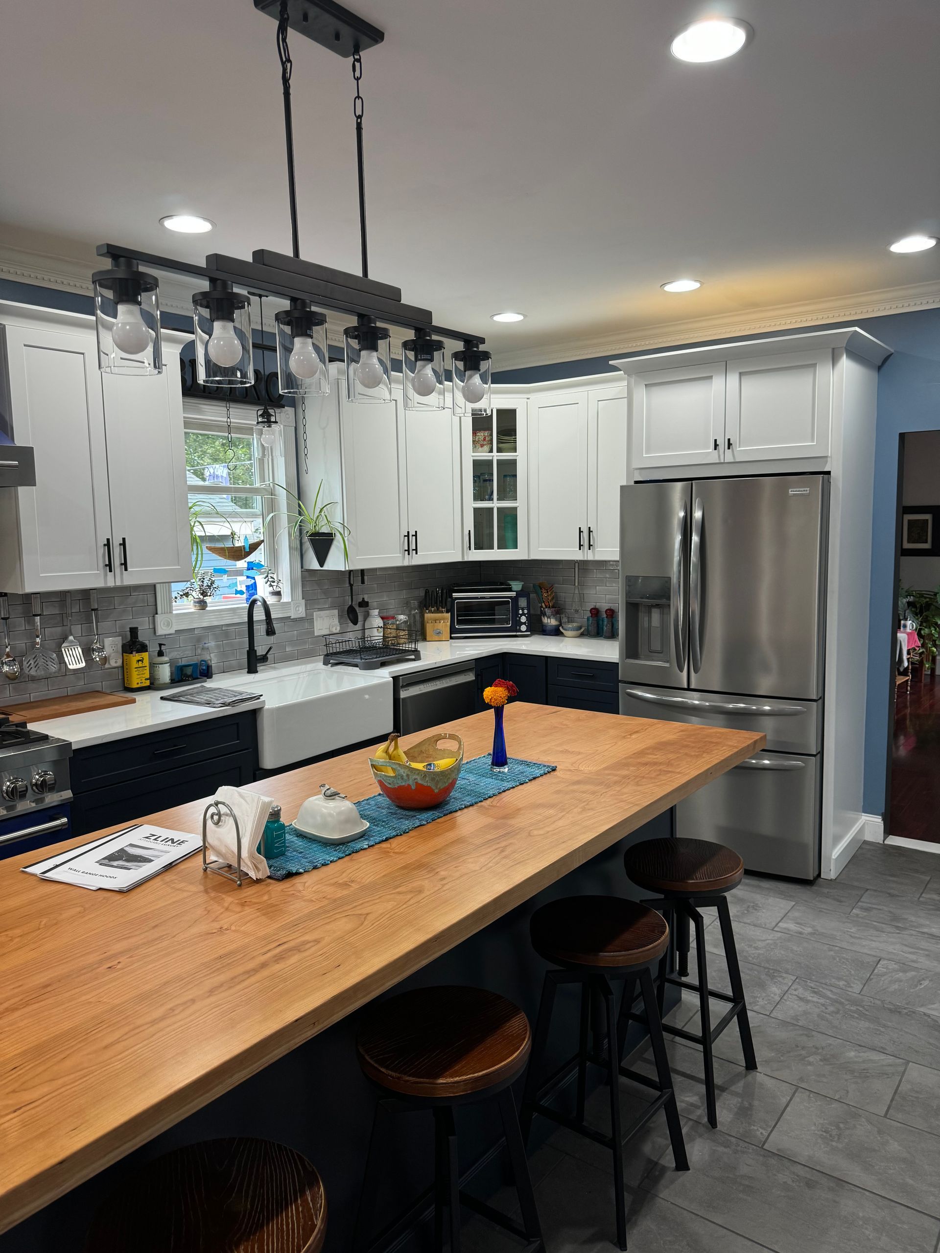 Modern kitchen with wood island, white and navy cabinets, stainless steel appliances, and a hanging light fixture.
