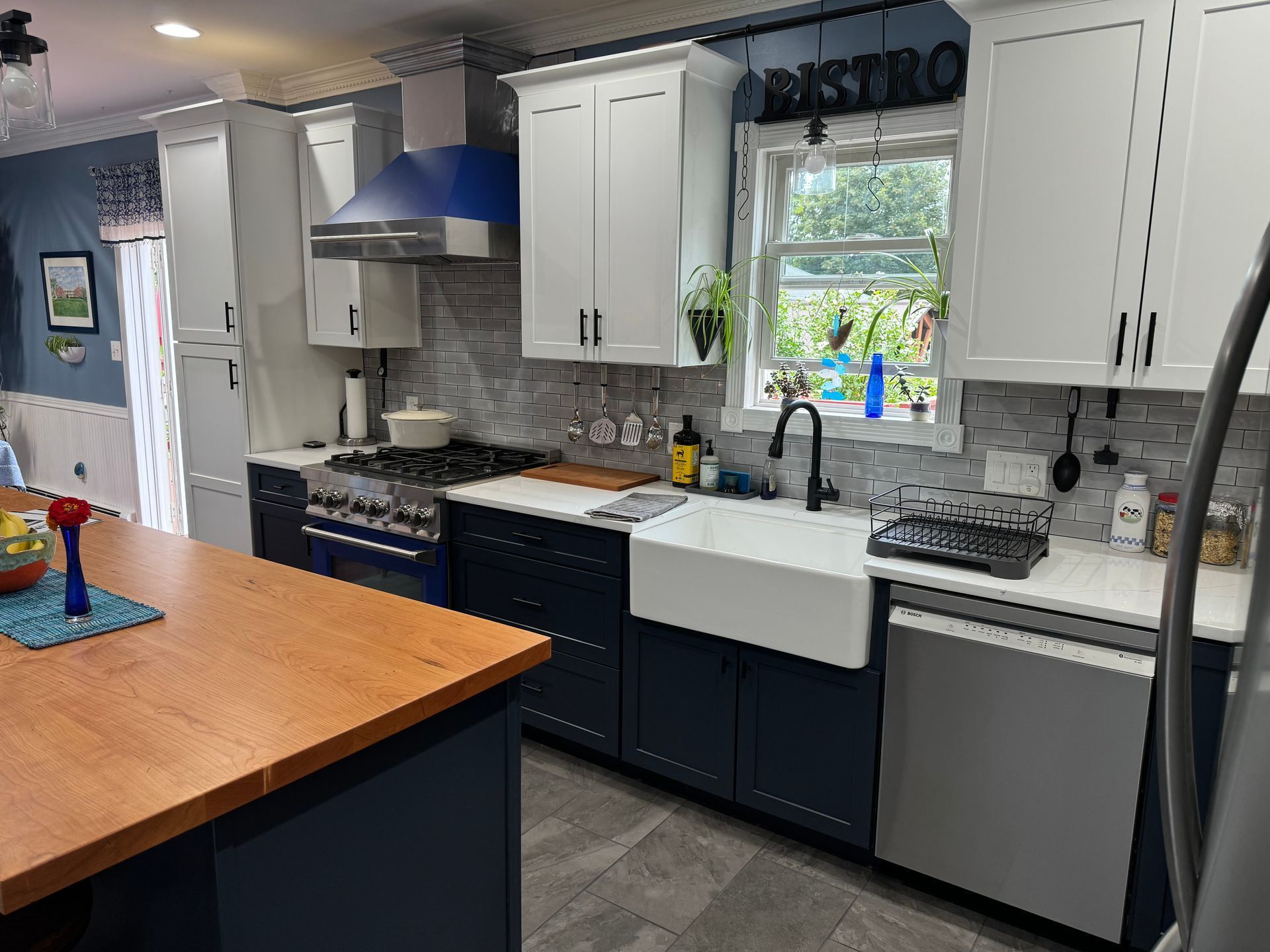 A kitchen with blue and white cabinets, stainless steel appliances, and a butcher block island.