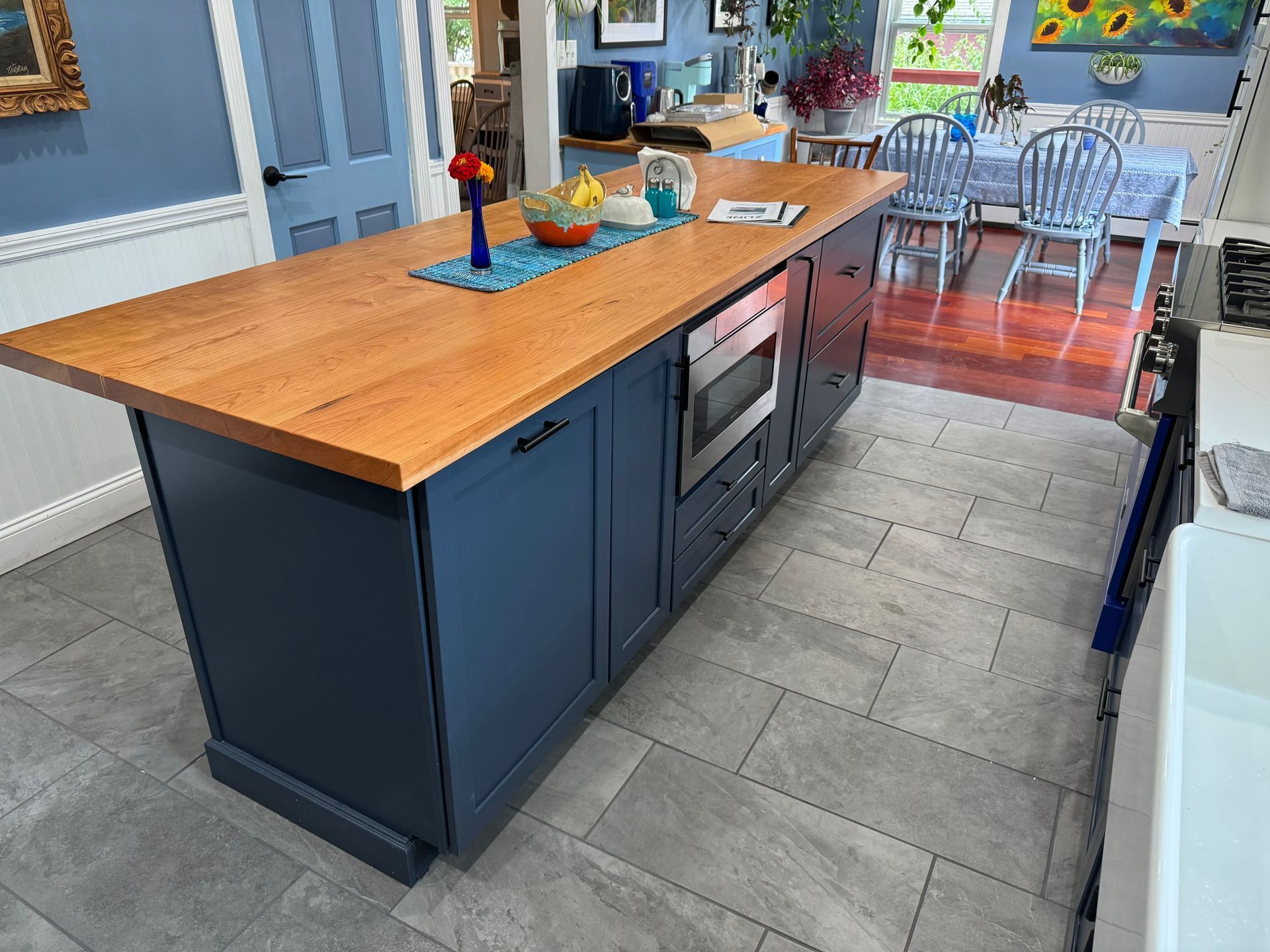Kitchen island with a wooden countertop and navy blue cabinets. Microwave built-in.