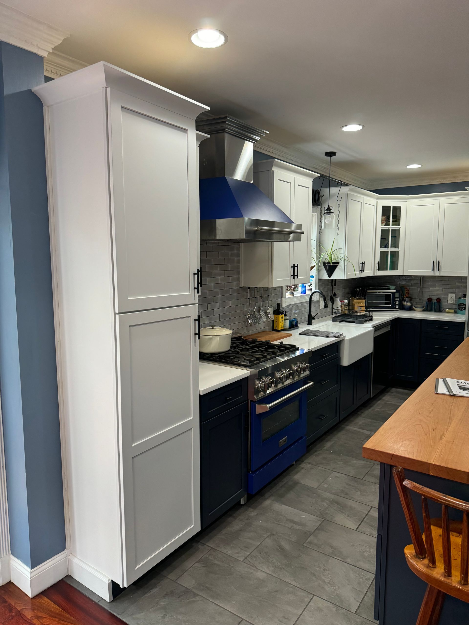 Kitchen with white cabinets, blue oven, range hood, and wood countertop.