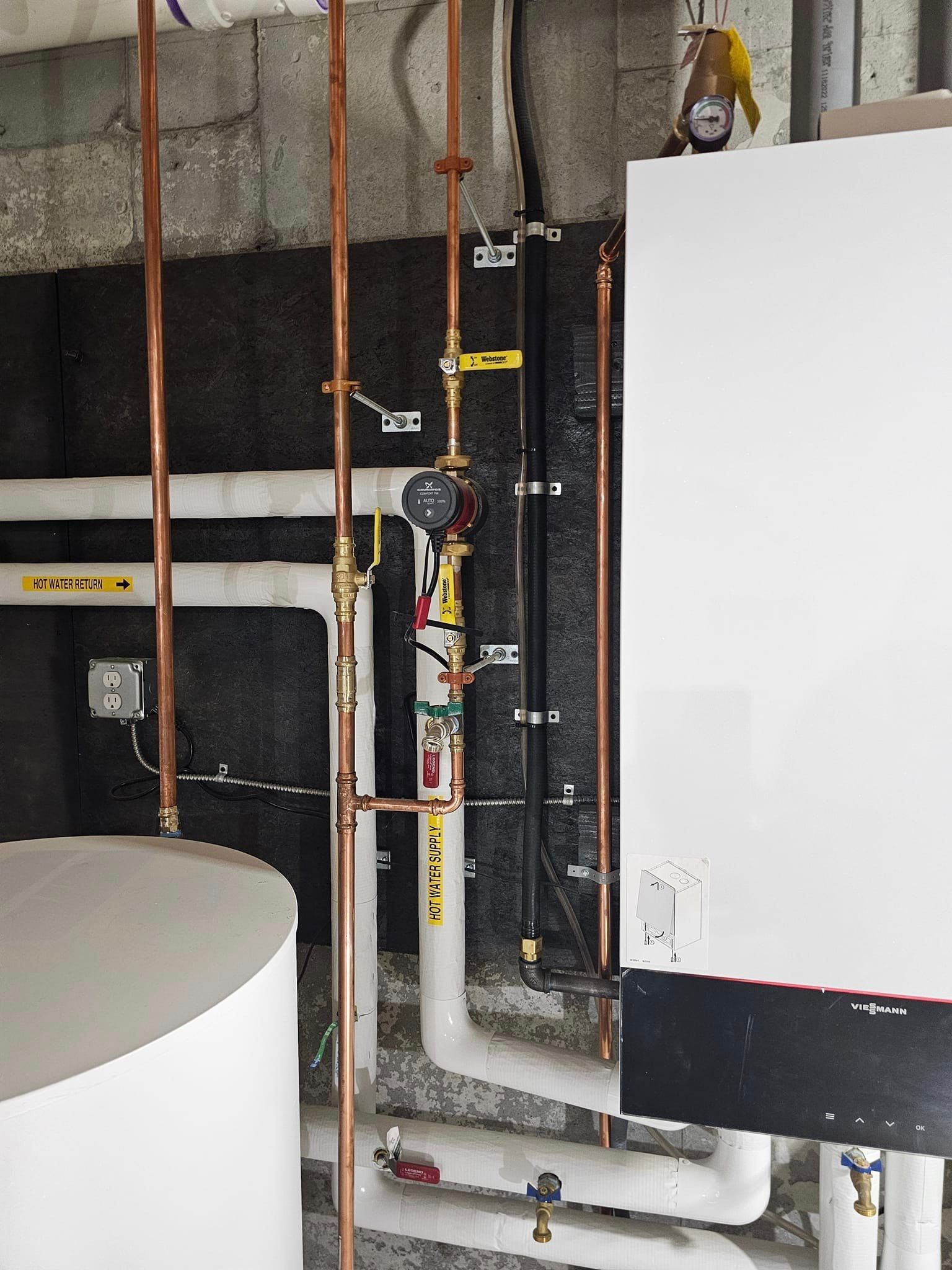 A white boiler is surrounded by copper pipes in a room
