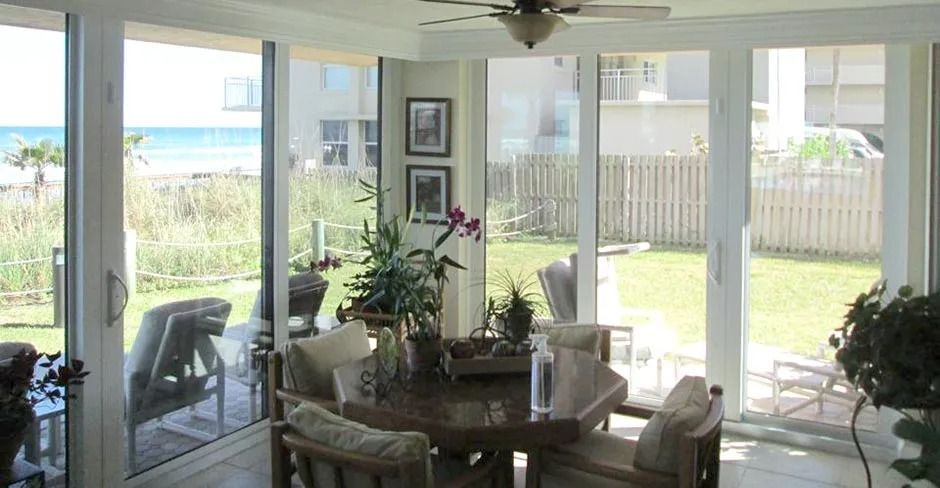 Sunroom with ocean and backyard views, table, chairs, and plants.