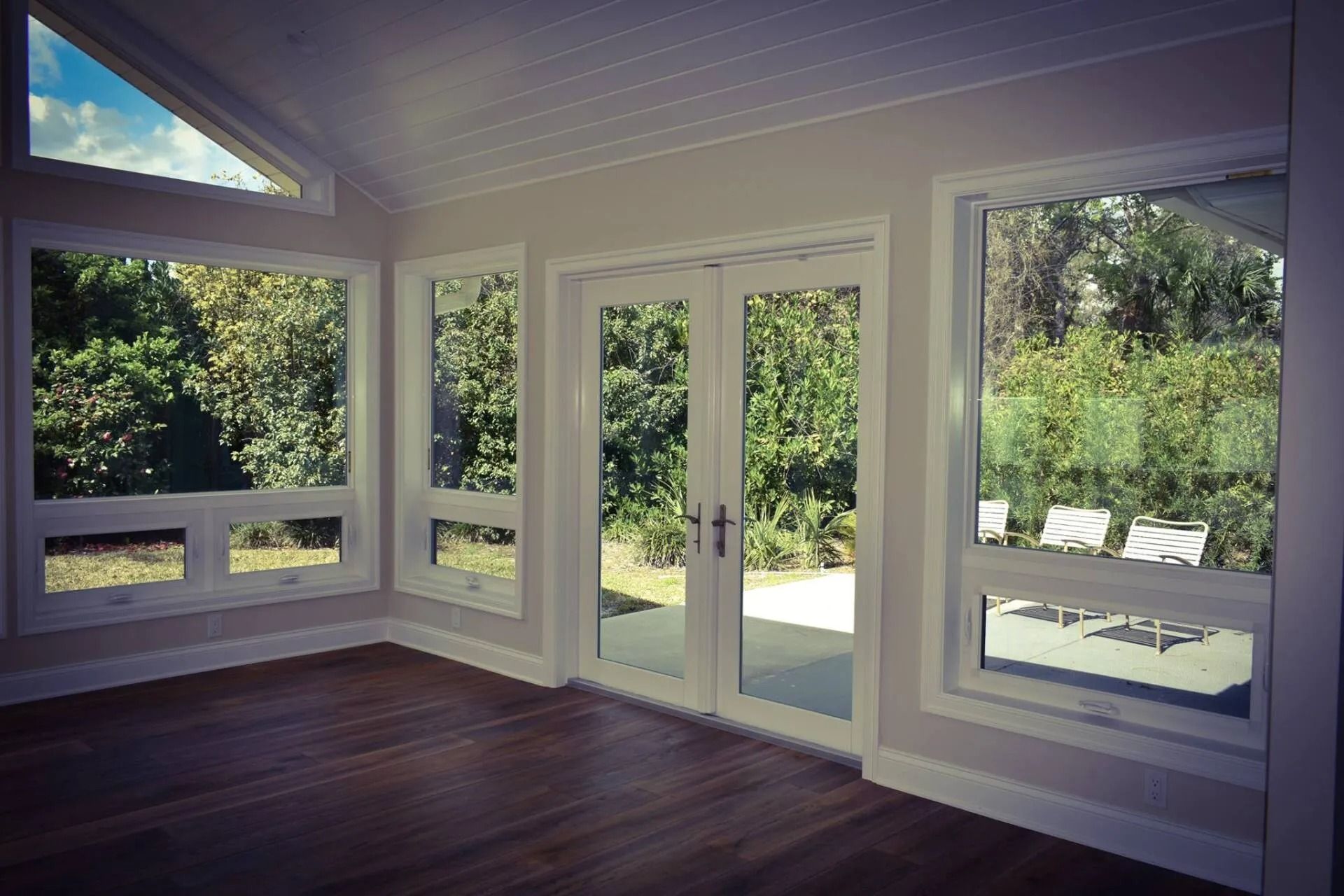 Interior room with large windows and French doors overlooking a lush backyard; hardwood floors.