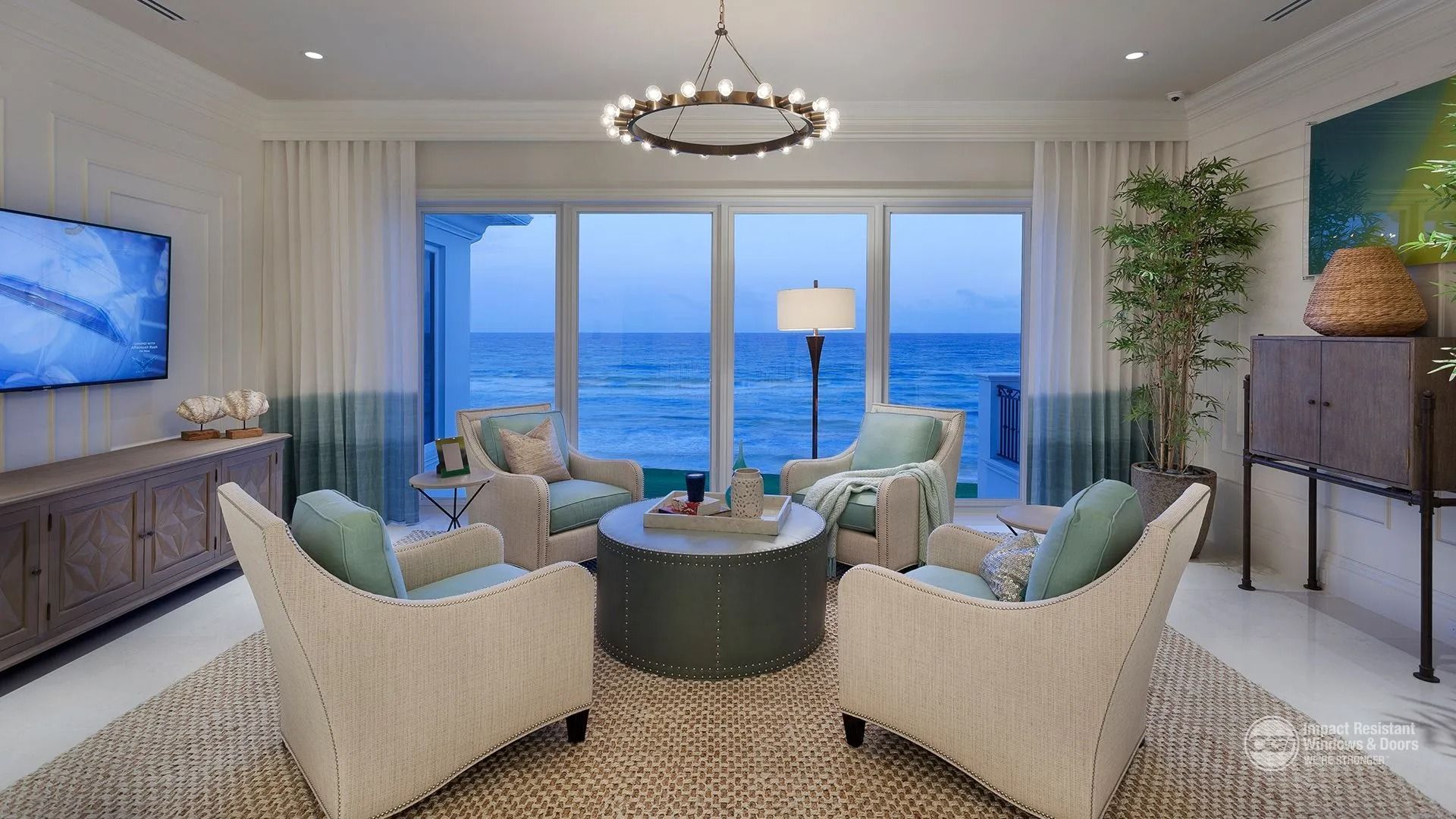 Living room with ocean view, four teal chairs around a central table, neutral rug, and a large window.