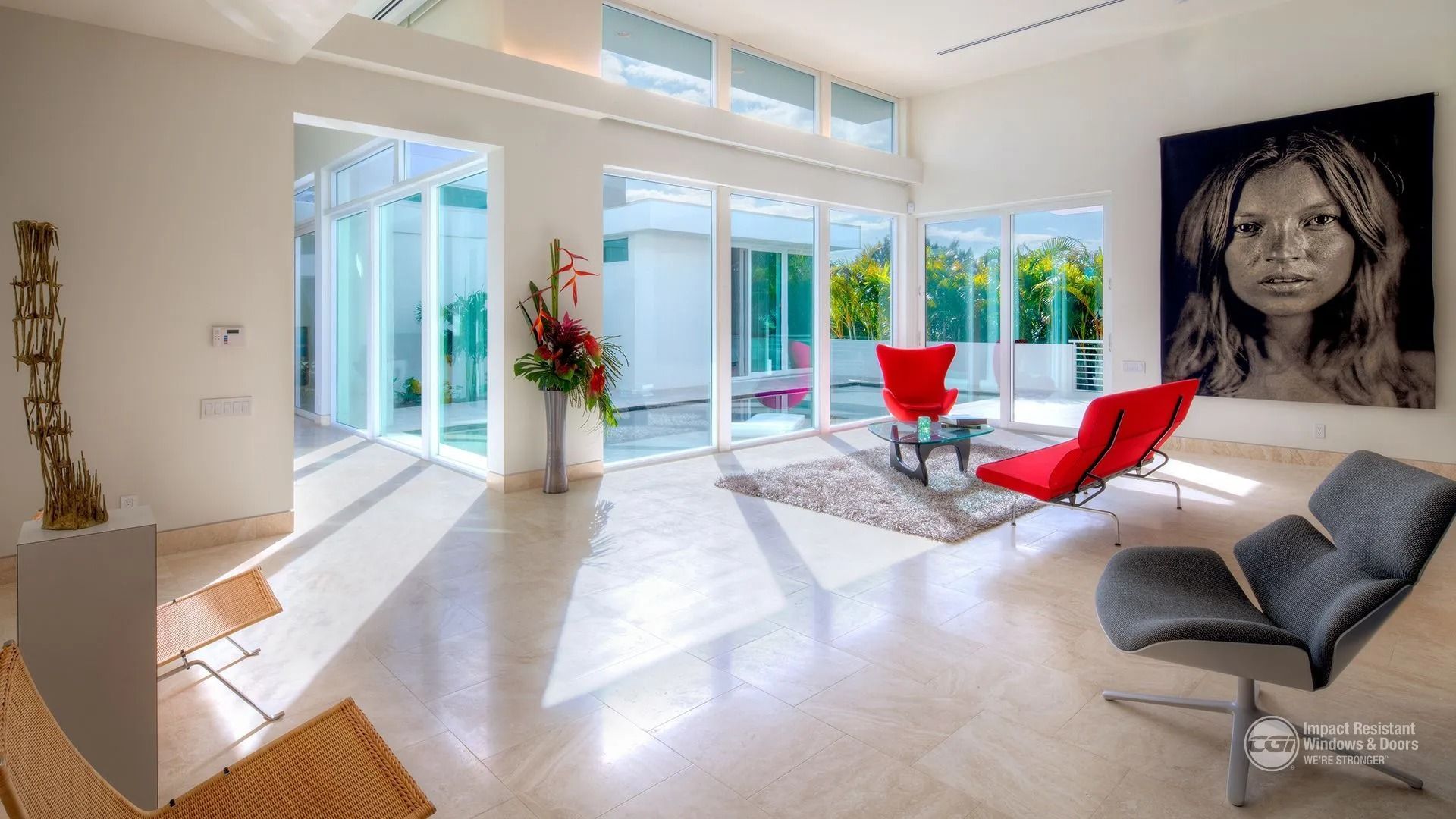 Modern living room with red chairs, large portrait, and view to a patio. Bright, open space.