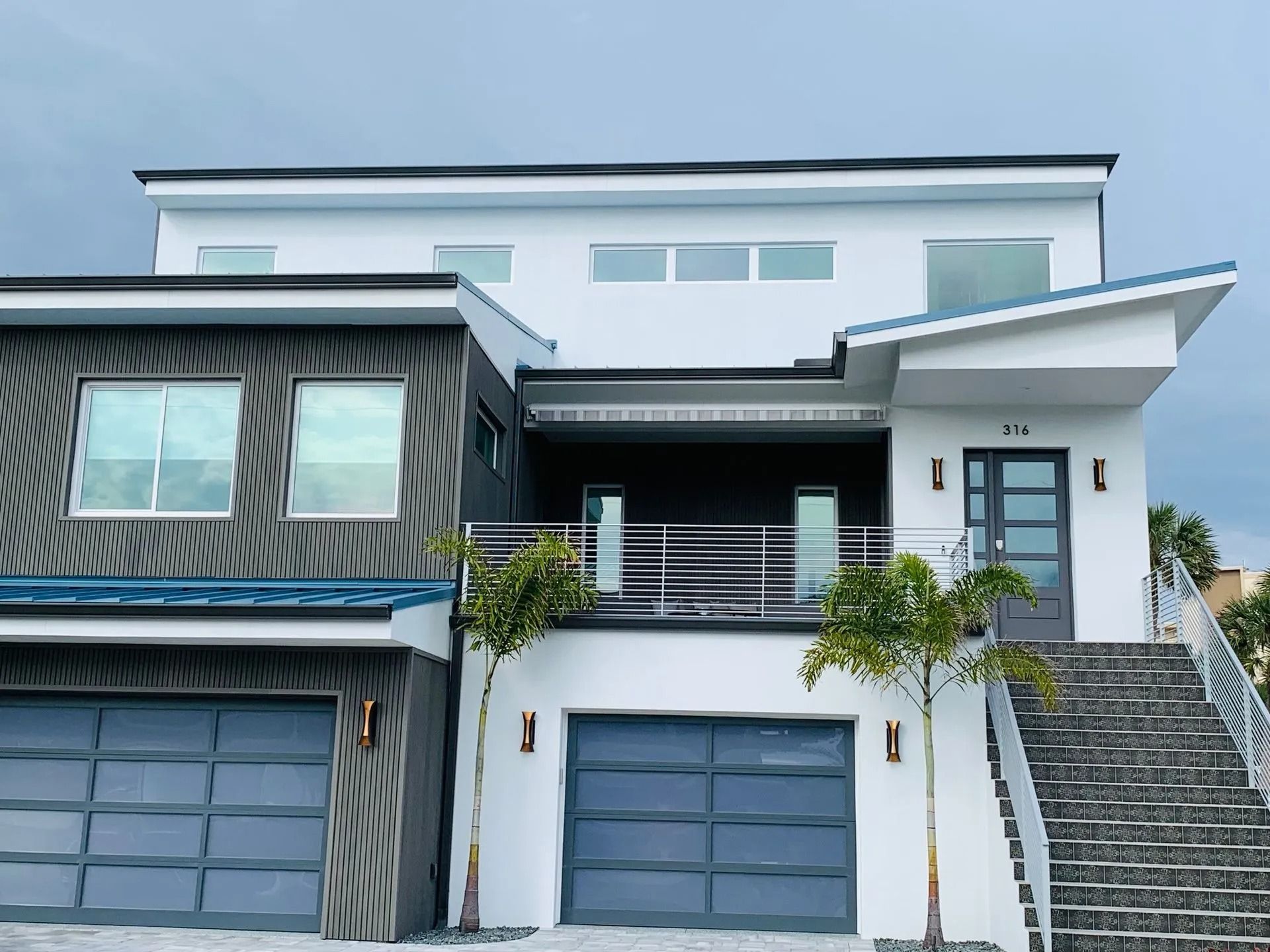 Modern two-story house with gray and white facade, balconies, and a staircase leading to the front door.