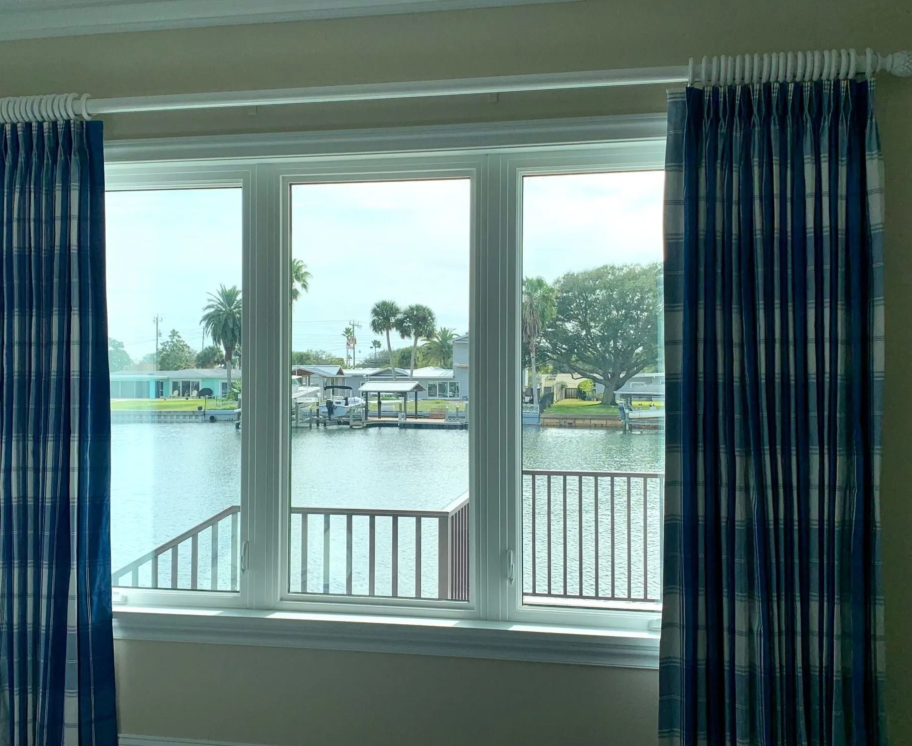 A large window looking out onto a calm canal with a dock, framed by floor-length dark blue and white striped curtains.