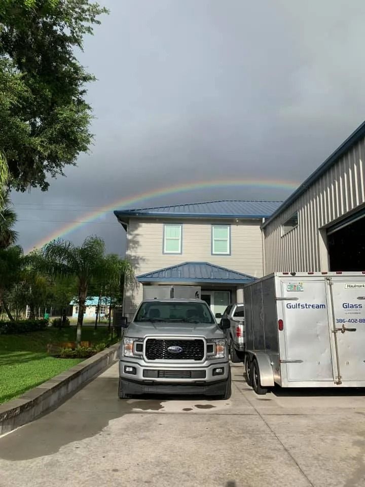 A silver Ford pickup truck parked in front of a building with a rainbow arching across the cloudy sky above.