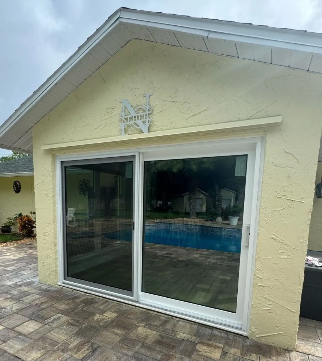 A yellow house exterior featuring large white sliding glass doors that reflect a backyard pool and patio area.