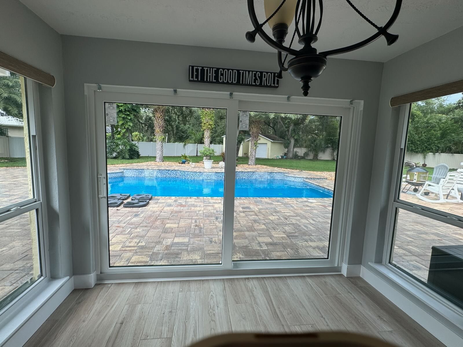 Room with pool view, large sliding glass doors, windows, and chandelier; “Let the good times roll” sign.