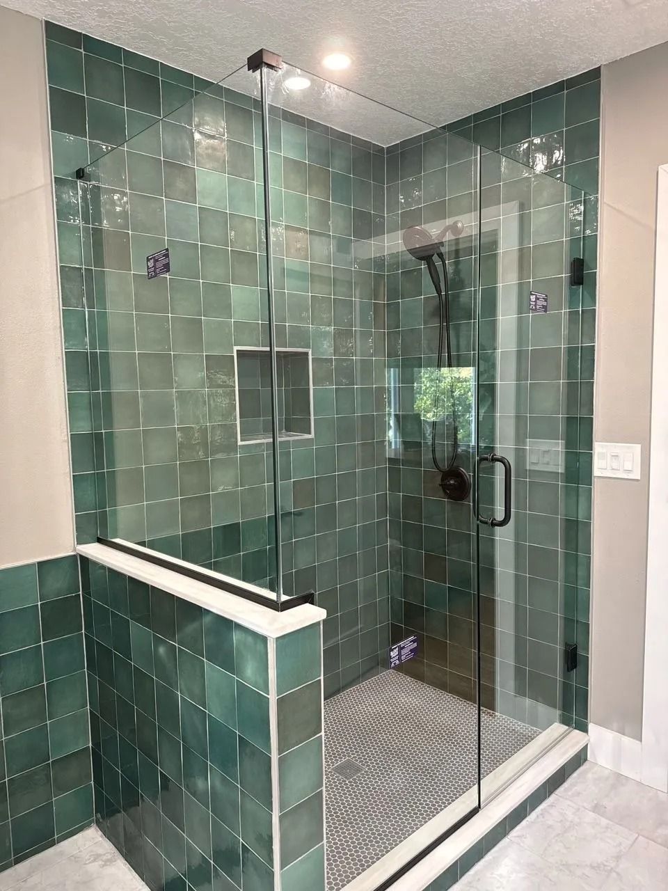 Green tiled shower with glass doors and a patterned floor.