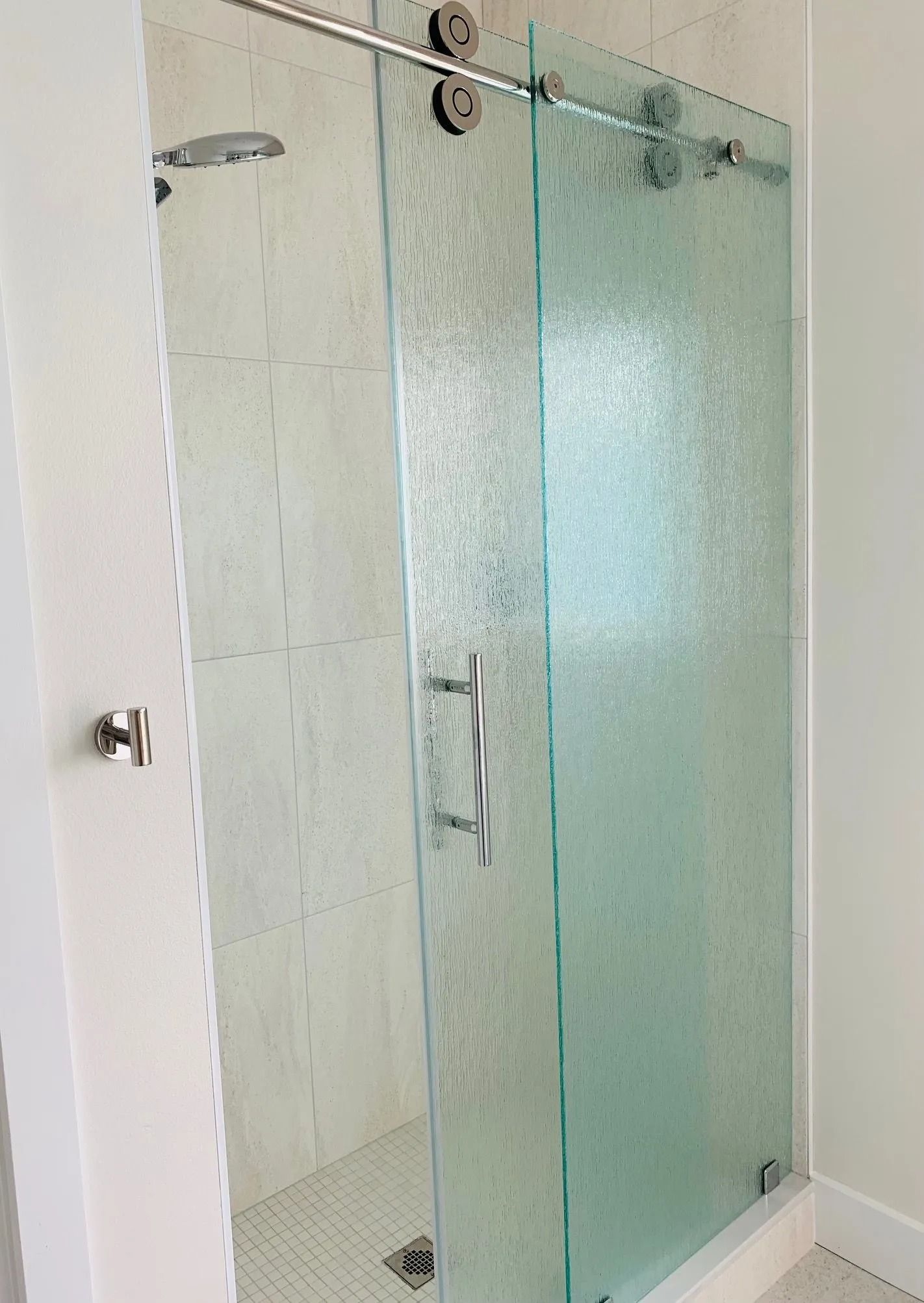 Shower with textured glass sliding door and chrome hardware in a white tiled bathroom.