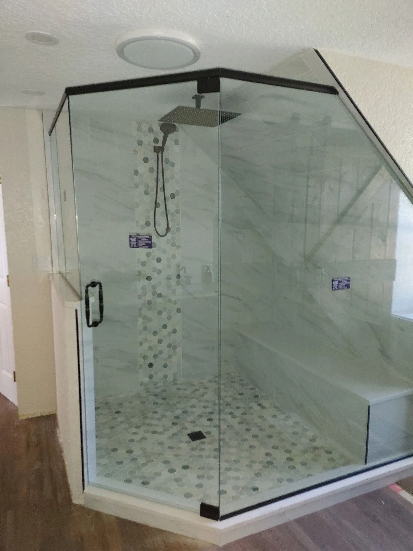 Corner shower with frameless glass doors, black trim, and marble-like tile.