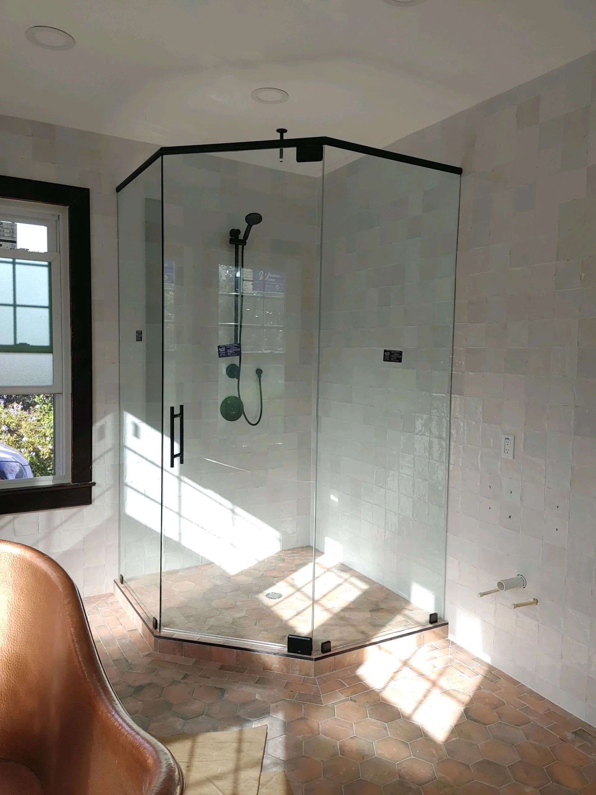 Corner glass shower enclosure with black trim in a bathroom with a window.