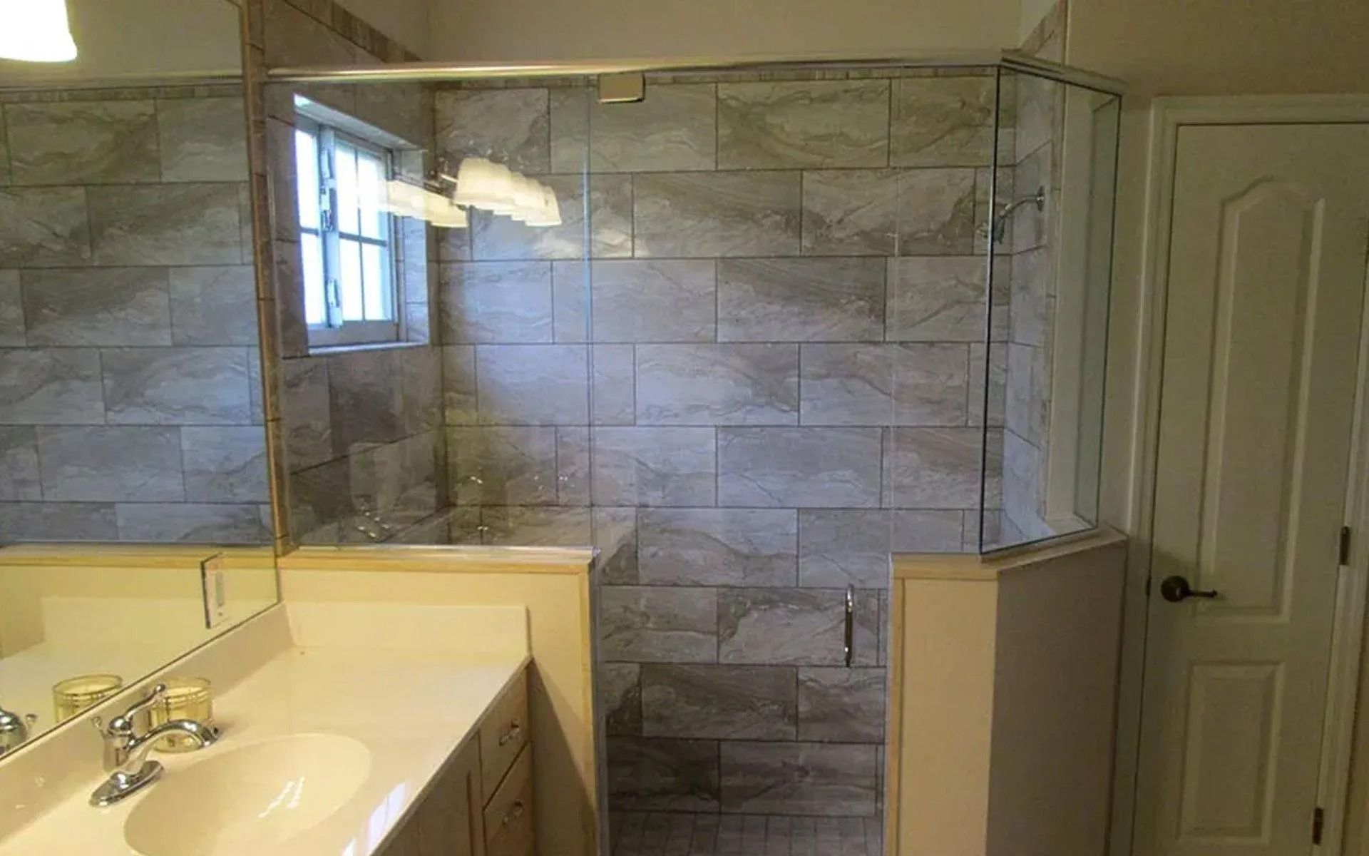 Bathroom with a glass shower enclosure and tiled walls. A vanity with a mirror and a closed door are on the left and right.