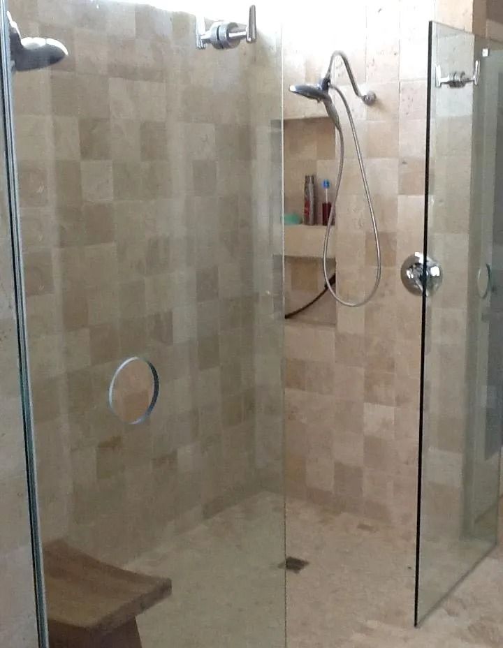 Glass-walled shower with two shower heads, stone tile walls, and a wooden bench.