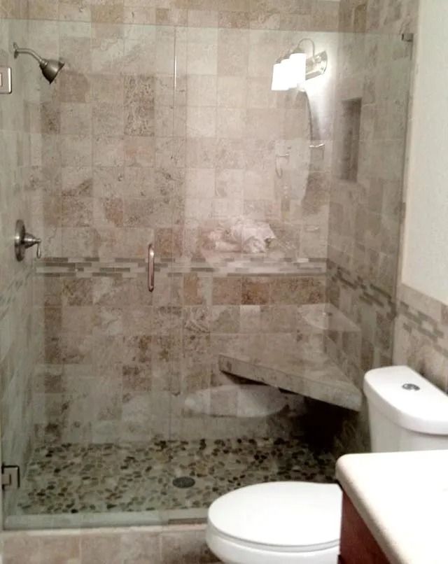 Shower with glass door, stone tile walls and pebble floor, built-in bench, and toilet next to it.