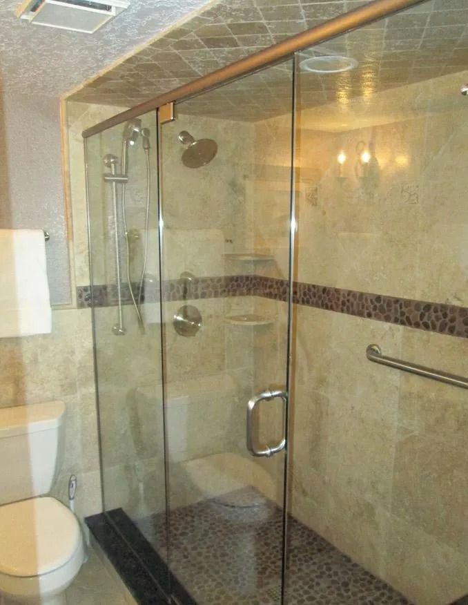 Bathroom with a clear glass shower door, beige tiled walls, and a toilet.