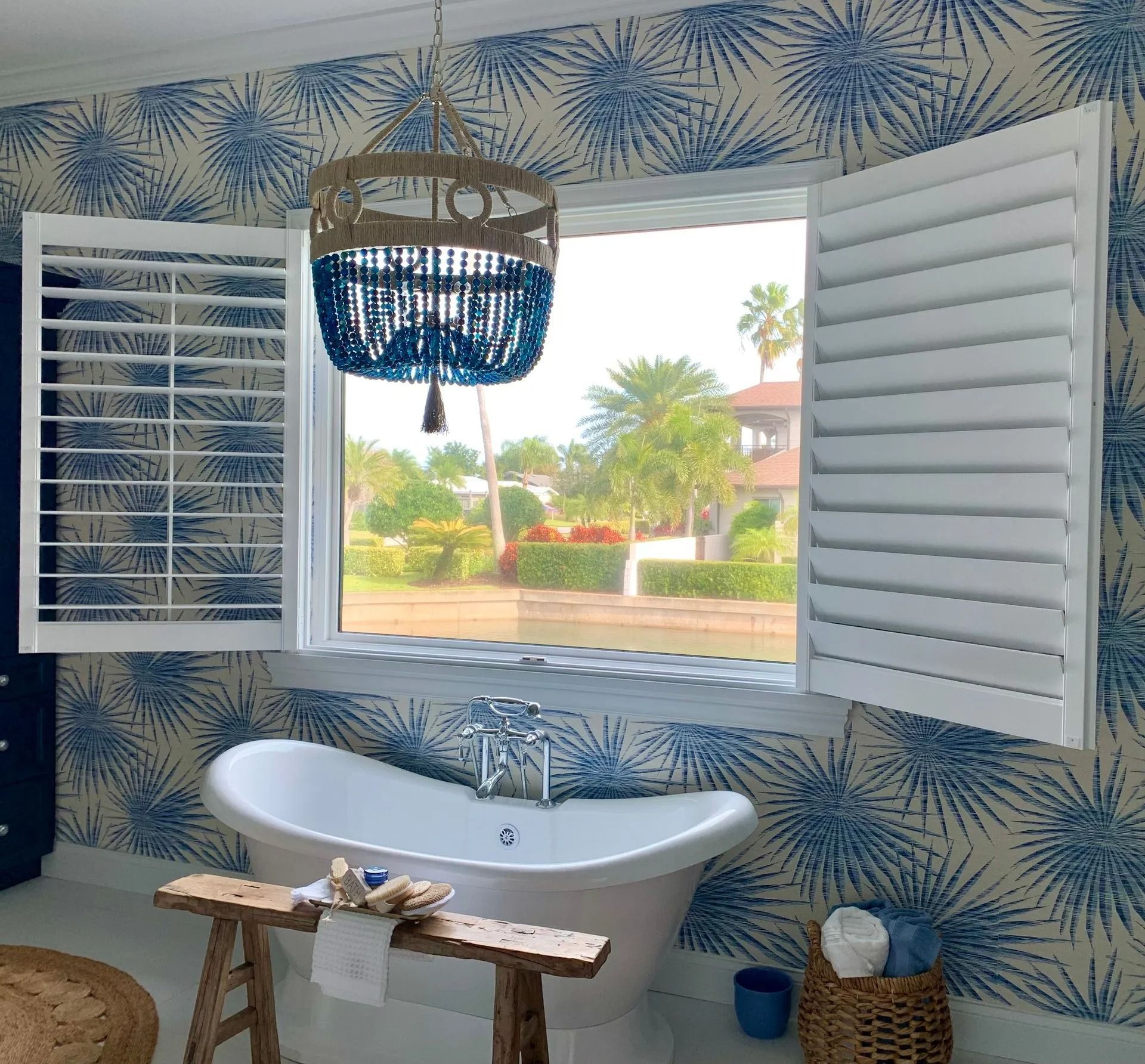 Bathroom with a white clawfoot tub, shutters, blue and white wallpaper, and a view of a green landscape.