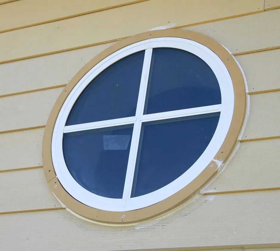 Oval window with white frame and grid, set in tan siding.