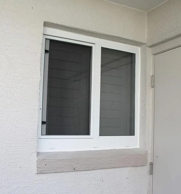 White-framed window with screen in a white stucco wall, adjacent to a white door.
