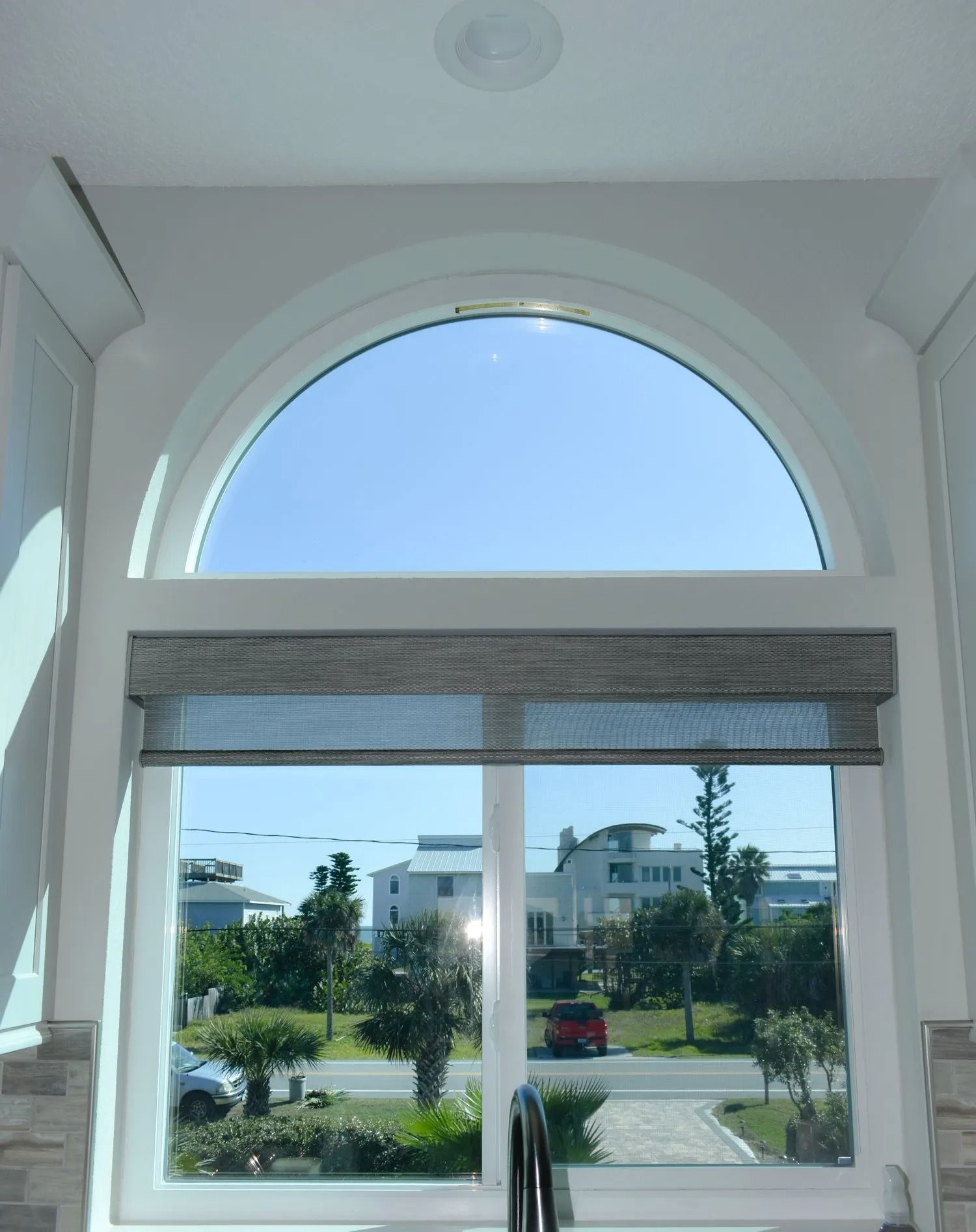 White arched window with a view of a street and buildings on a sunny day.