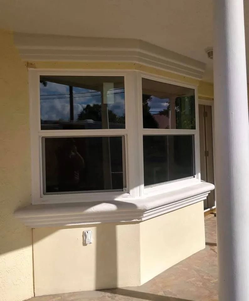 White-framed bay window on a yellow stucco wall, with a decorative white trim.