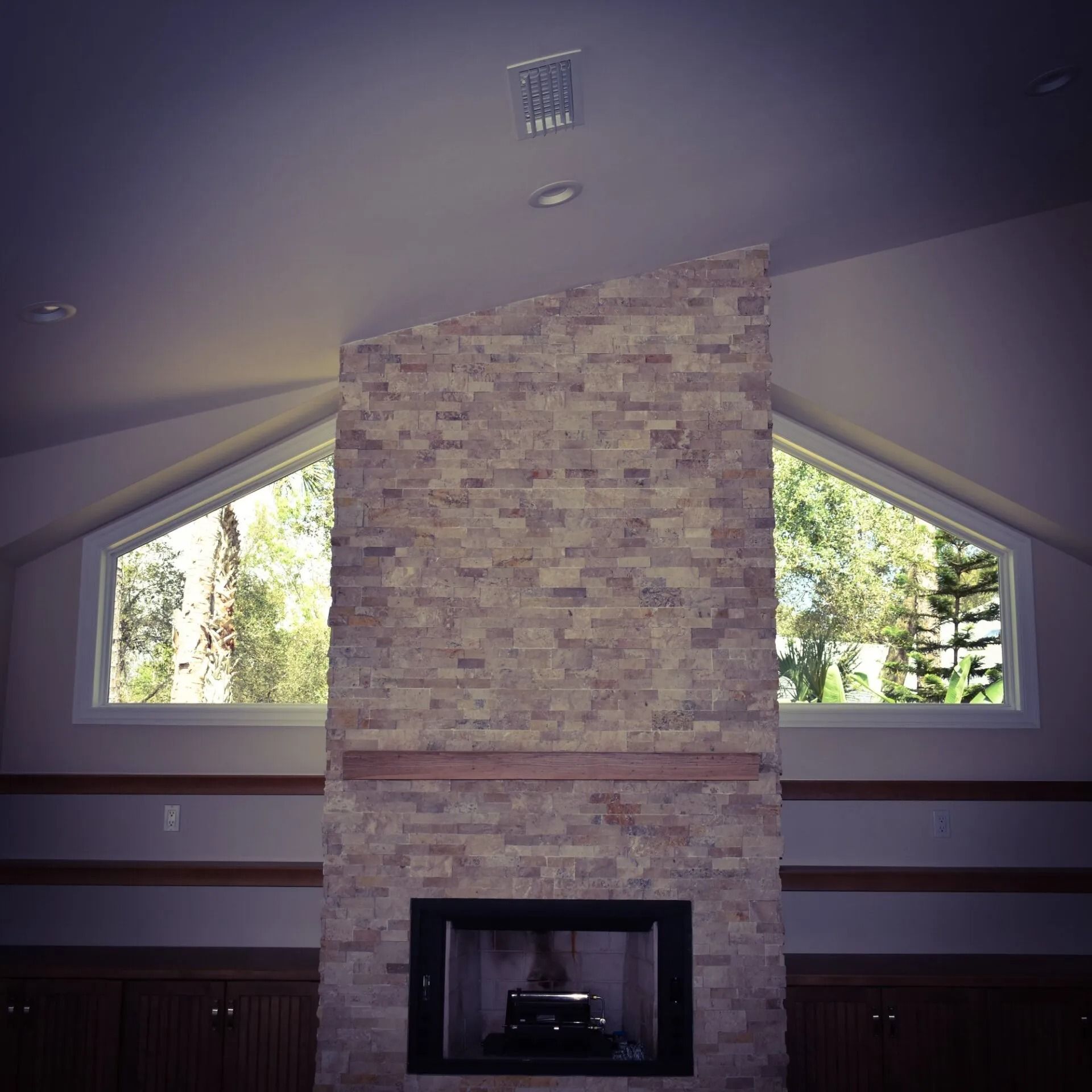 Fireplace with stone facade between two triangular windows; a dark fireplace opening is centered.