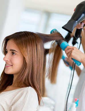Woman getting hair styled with a blow dryer and round brush at a salon.