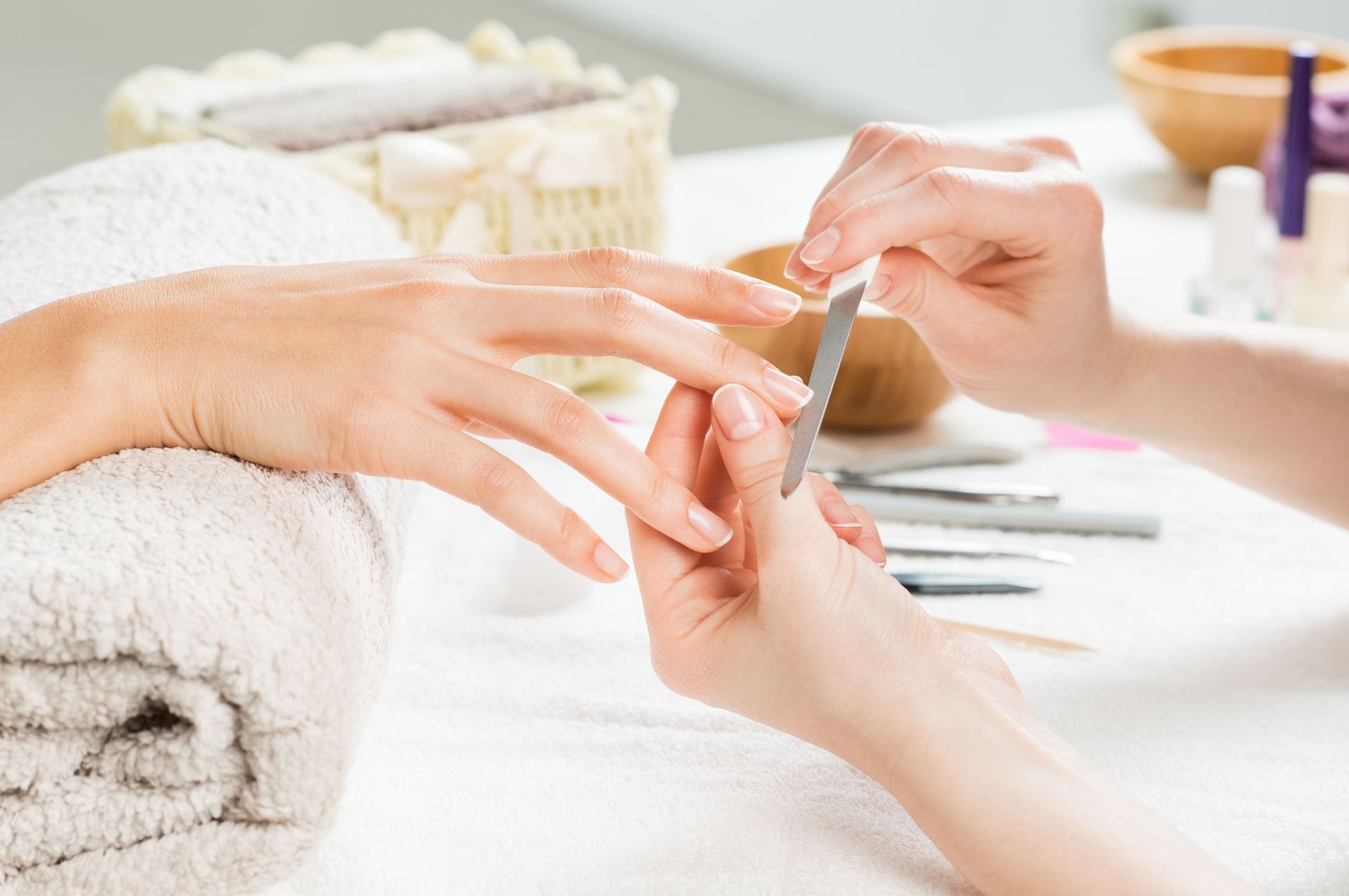 Person filing another person's fingernails at a manicure table with towels and tools.