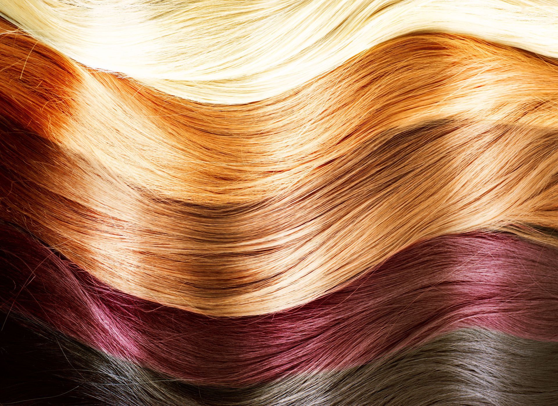 Close-up of wavy strands of hair in various shades, including blonde, copper, and dark red.