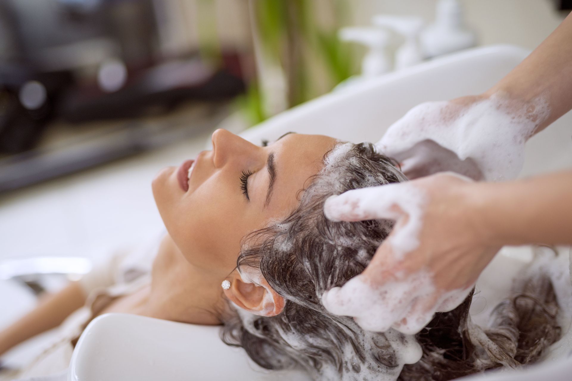 Woman getting her hair washed at a salon, white foam suds, eyes closed, head back.