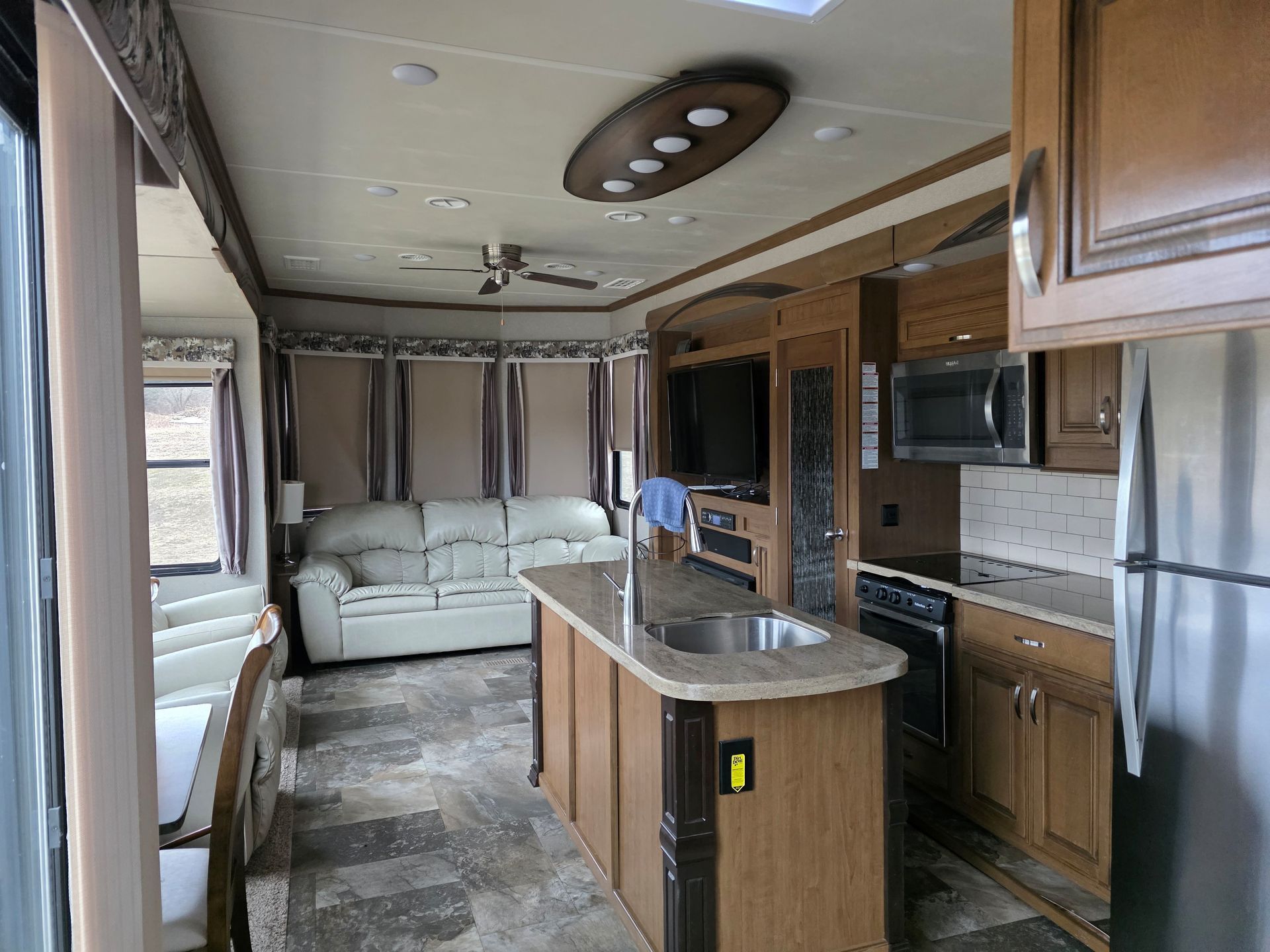 Interior of a motorhome kitchen and living area with wood cabinets, white sofa, and countertop island