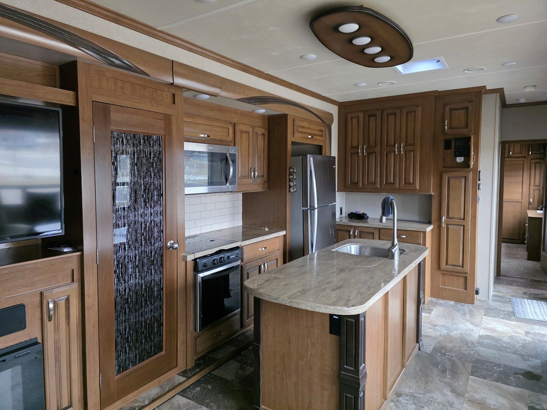 Wood-paneled kitchen interior with island, stainless appliances, and beige countertops