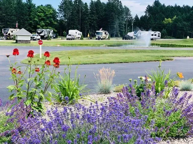 RV park with flower bed in foreground and RVs in the background, a fountain, and trees.