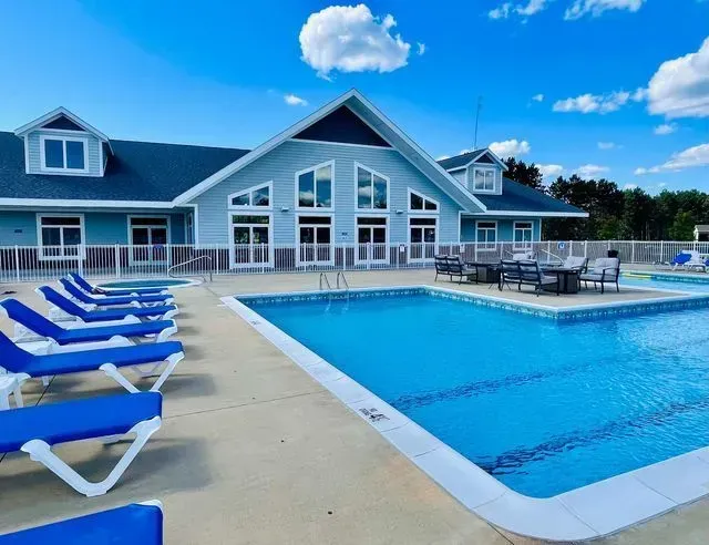 Blue pool and lounge chairs in front of a blue building with glass doors, under a blue sky.